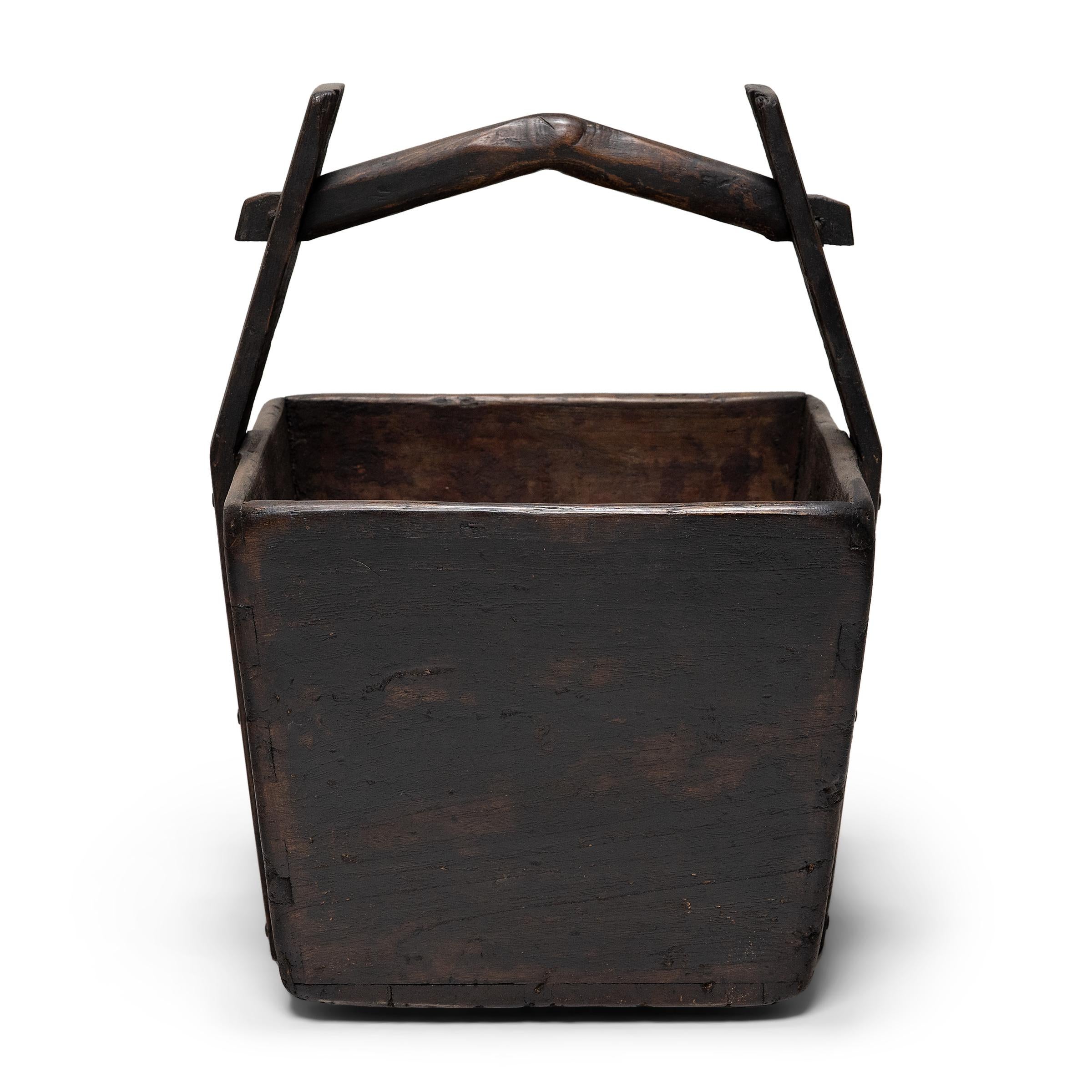 This hand-crafted wooden bucket was once used by farmers in Shanxi, China to transport their harvest of rice and grains over long distances. Counterbalanced by a second container, the pail would have been lifted by a pole threaded through the tall