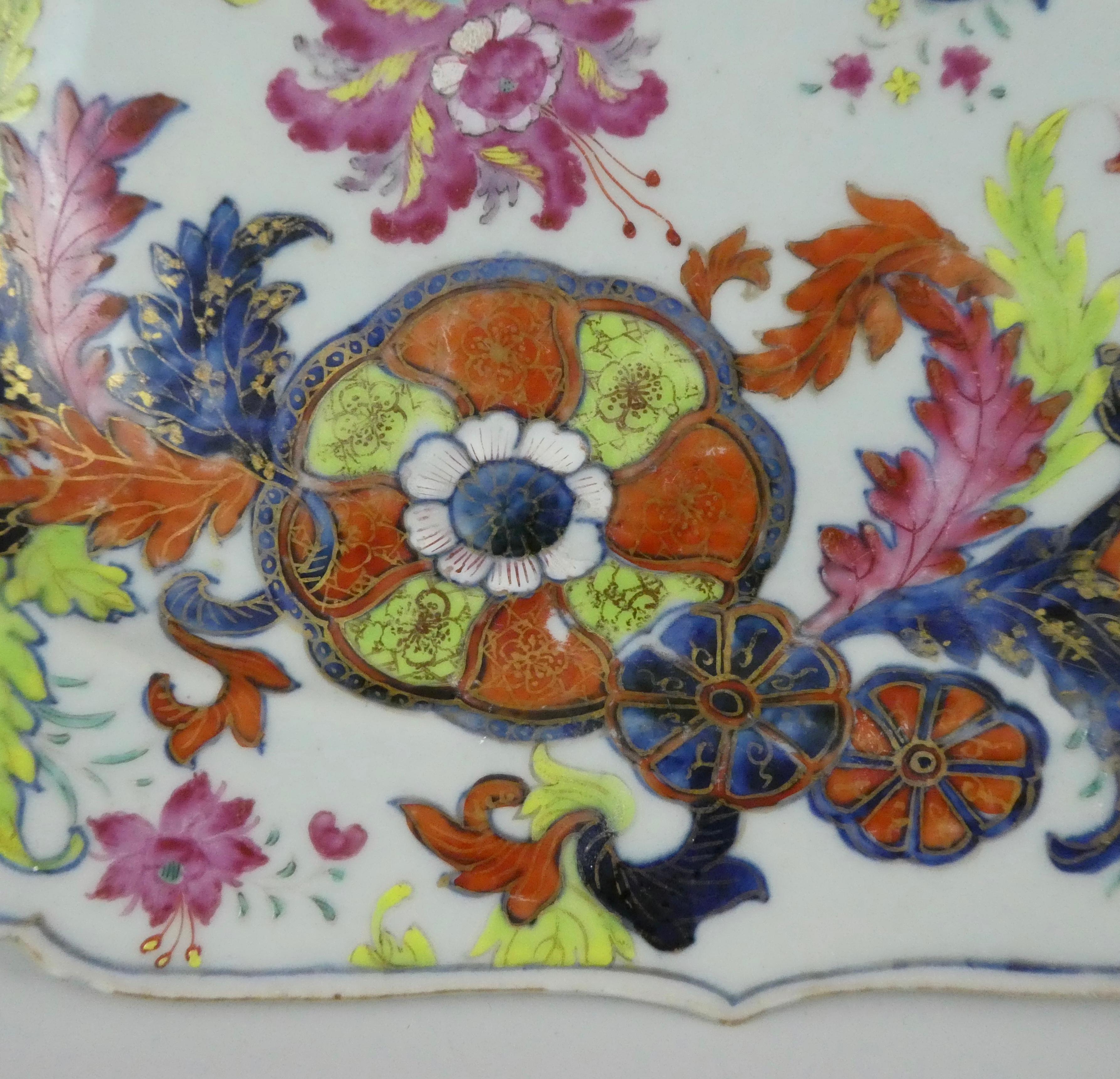 A Chinese porcelain dish, painted in the ‘Pseudo Tobacco Leaf’ Pattern, Qianlong Period, circa 1760. The rectangular dish having a foliage molded rim, and painted in famille rose enamels, with pink hibiscus blooms, amongst stylized cut fruit, and