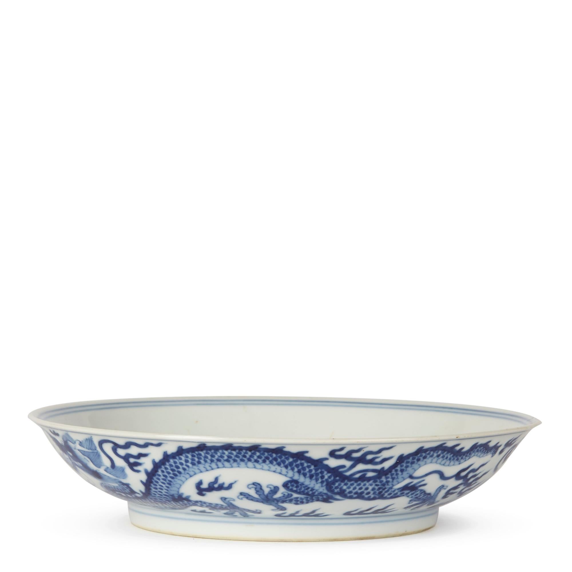 A stunning and rare Chinese Qianlong porcelain blue and white shallow dish finely decorated with a central five claw imperial dragon chasing a flaming pearl through clouds. The pattern is repeated around the outside rim of the dish with simple line