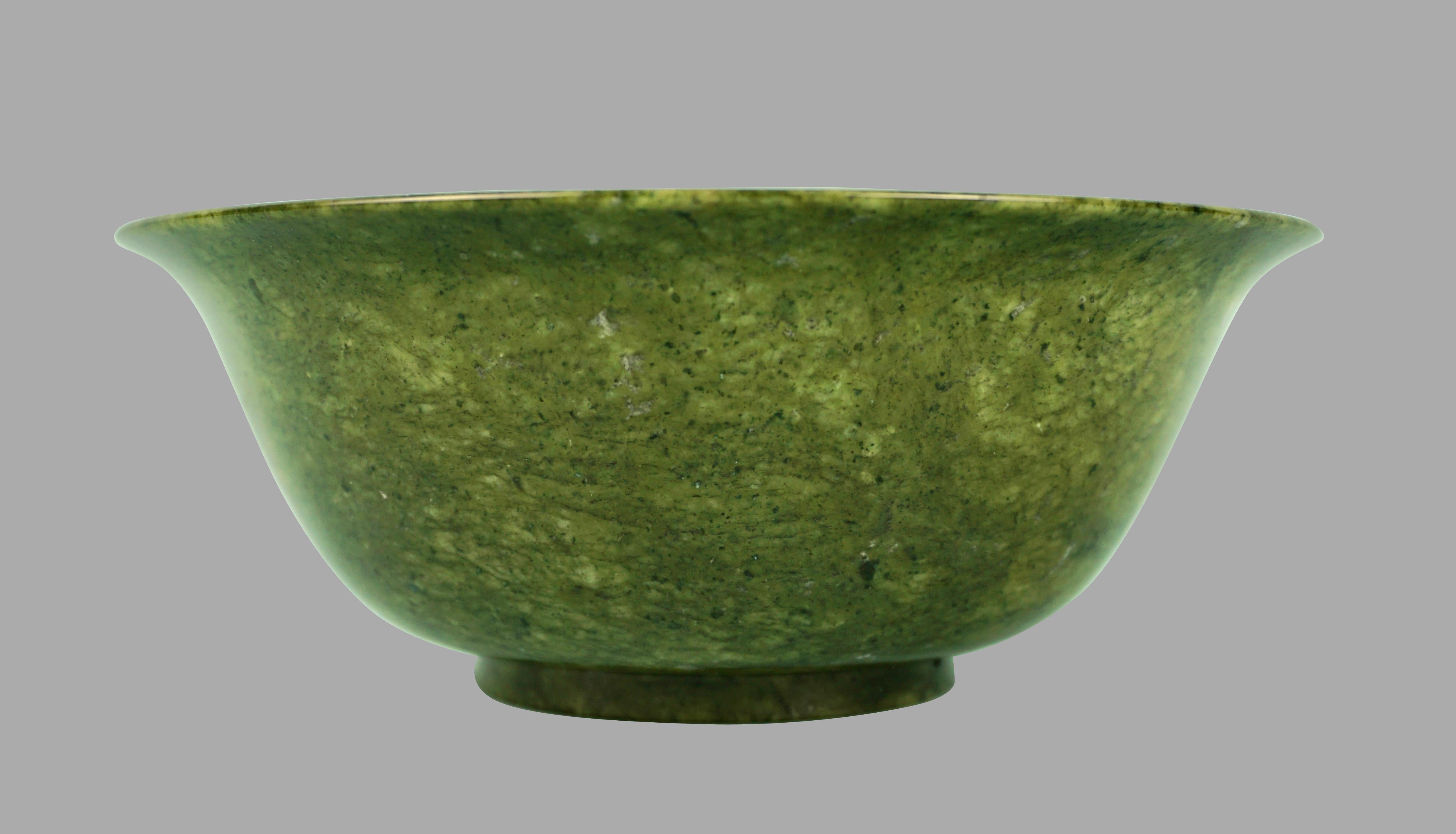 A well-carved Chinese Qianlong style jade footed bowl of typical form with curved sides and a gently flaring mouth rim. The stone is a spinach green tone with speckled black and white inclusions. An elegant and restrained piece. Probably 20th