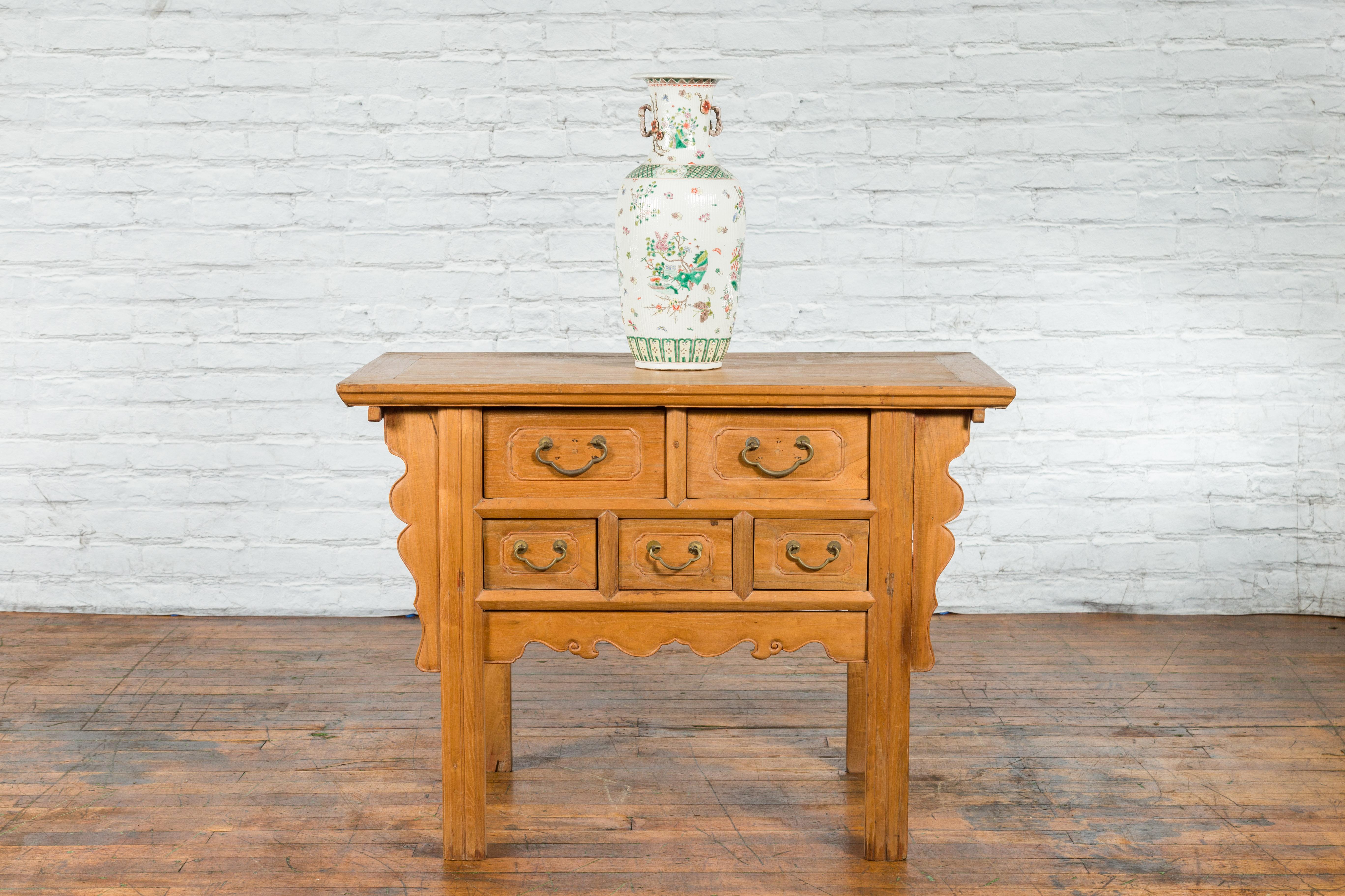 A Chinese Qing Dynasty period side table from the 19th century, with five drawers, carved apron and bronze hardware. Created in China during the Qing Dynasty, this side table captures our attention with its elegant silhouette and warm patina. The