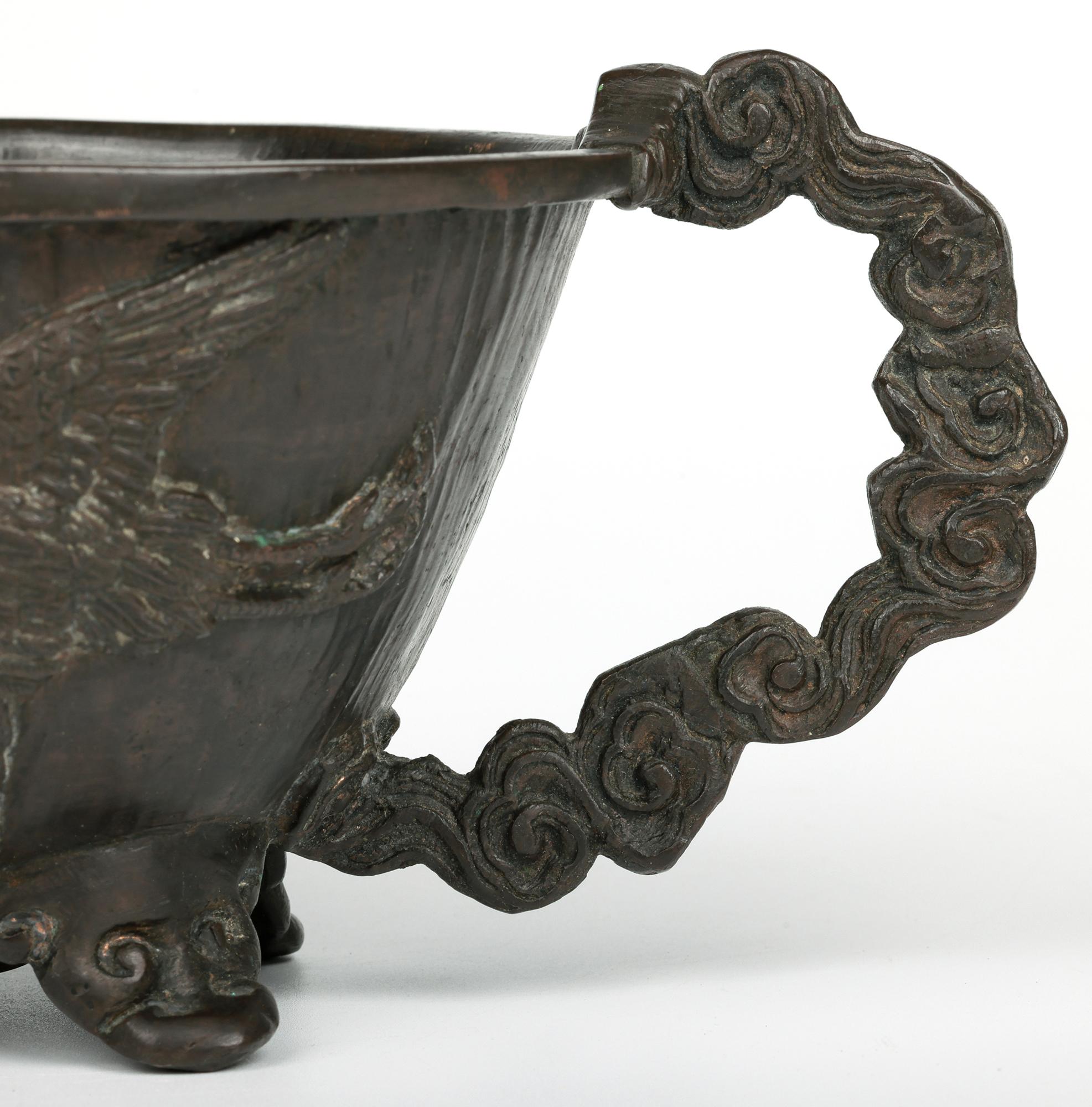 Elegante e impresionante salsera antigua china Qing de bronce decorada con grullas y que data del siglo XIX. La salsera, de estilo arcaico, se eleva sobre tres pies de mascarón moldeados y tiene forma ovalada, con un pitorro extendido en un extremo