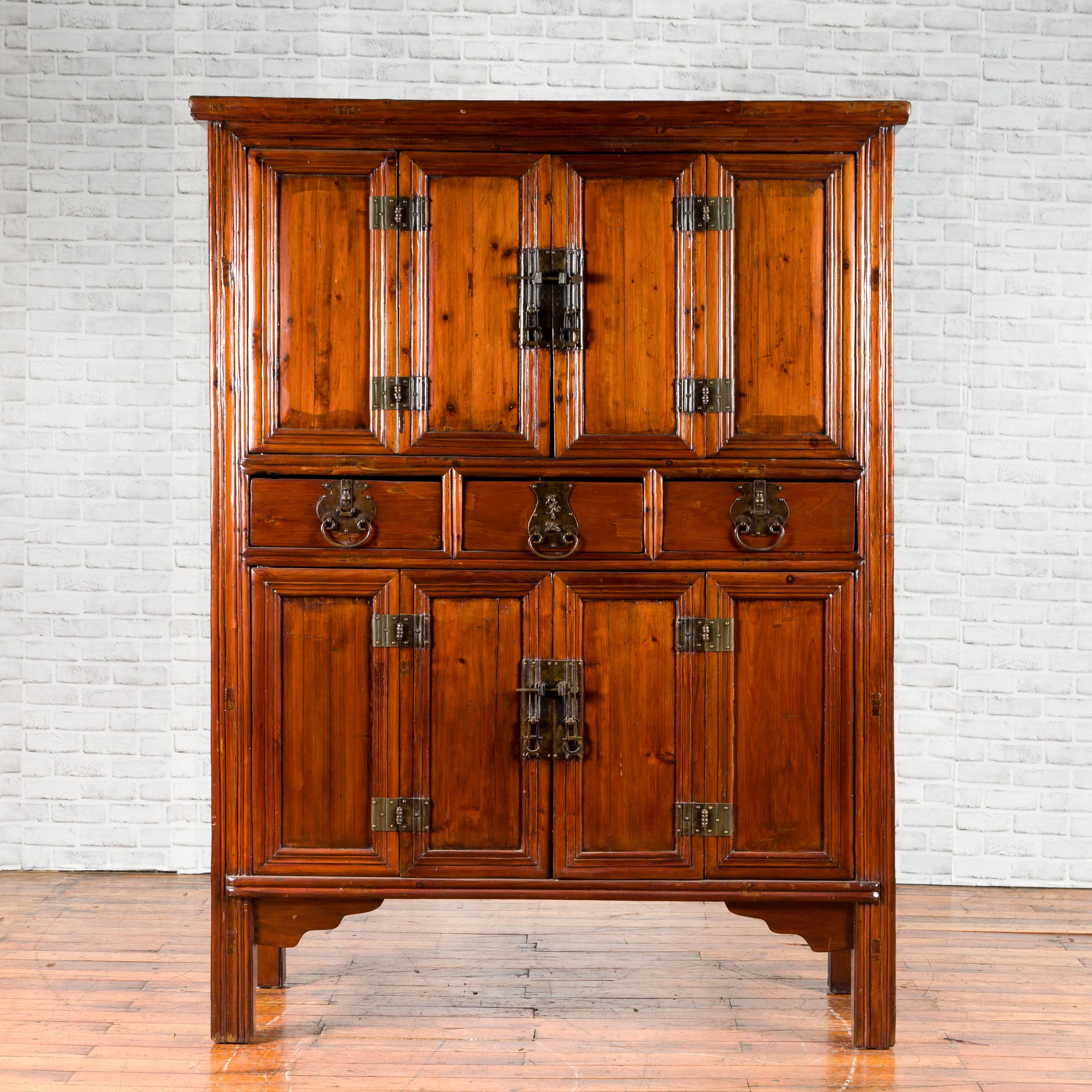 A Chinese Qing Dynasty period four accordion door cabinet from the 19th century, with three drawers and brass hardware. Created in China during the Qing Dynasty, this brown cabinet features two pairs of accordion doors fitted with brass hardware,