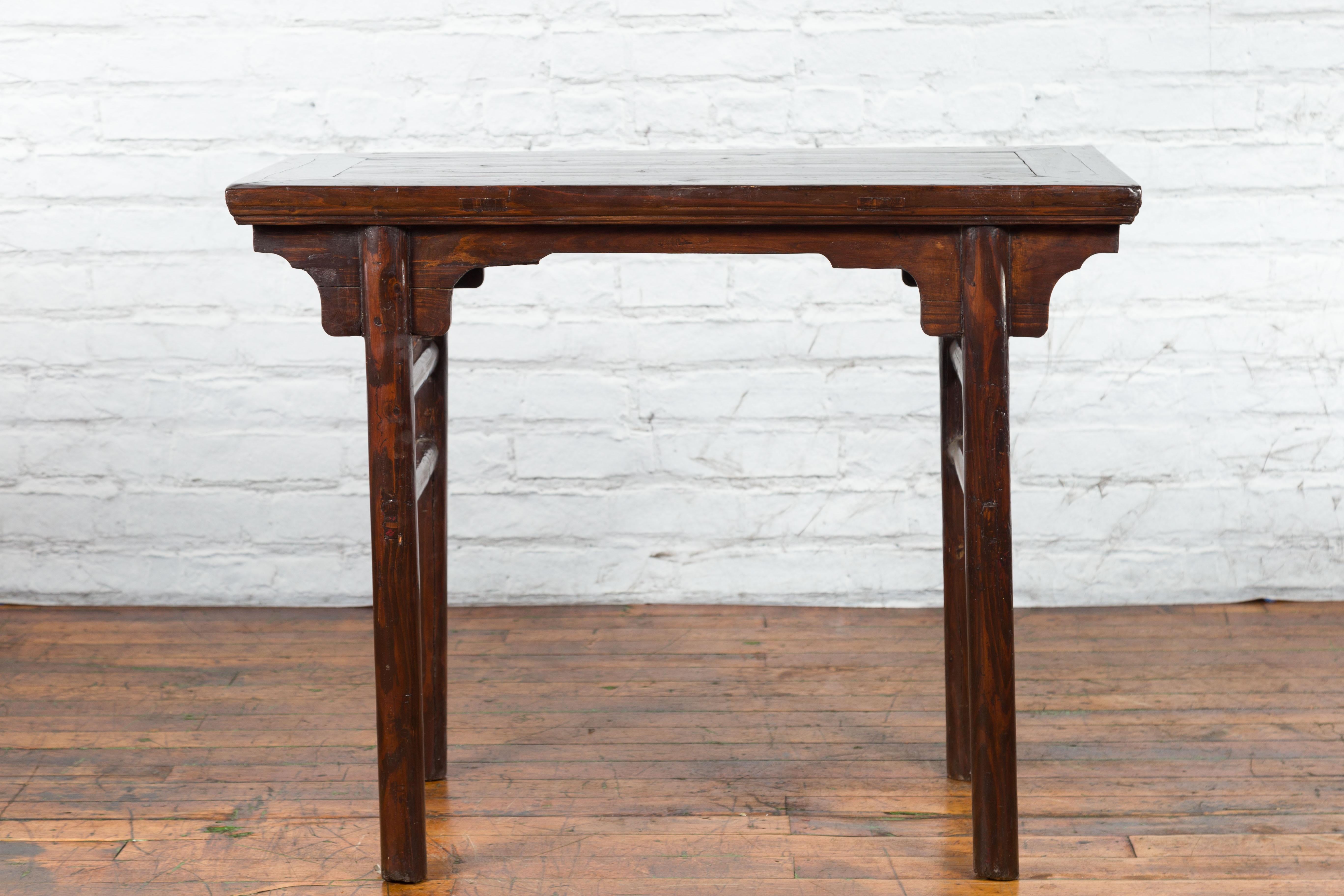 A Chinese Qing Dynasty period altar console table from the 19th century with carved spandrels and side stretchers. Created in China during the Qing Dynasty, this wooden altar table features a rectangular top with central board, sitting above four