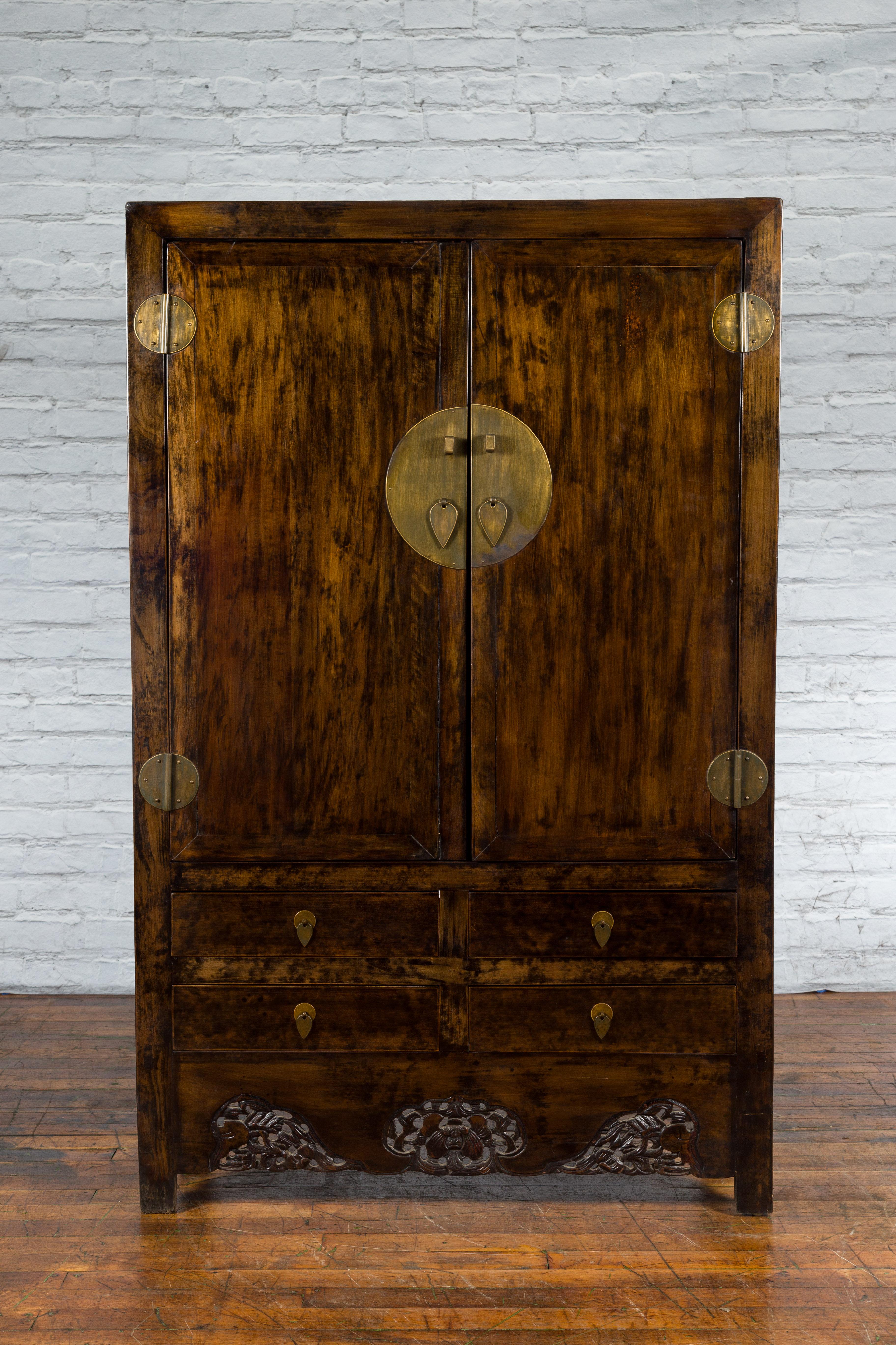 A Chinese Qing Dynasty period wooden armoire from the 19th century with carved skirt, brown patina and large brass medallion. Created in China during the Qing Dynasty in the 19th century, this wooden armoire features a linear silhouette perfectly