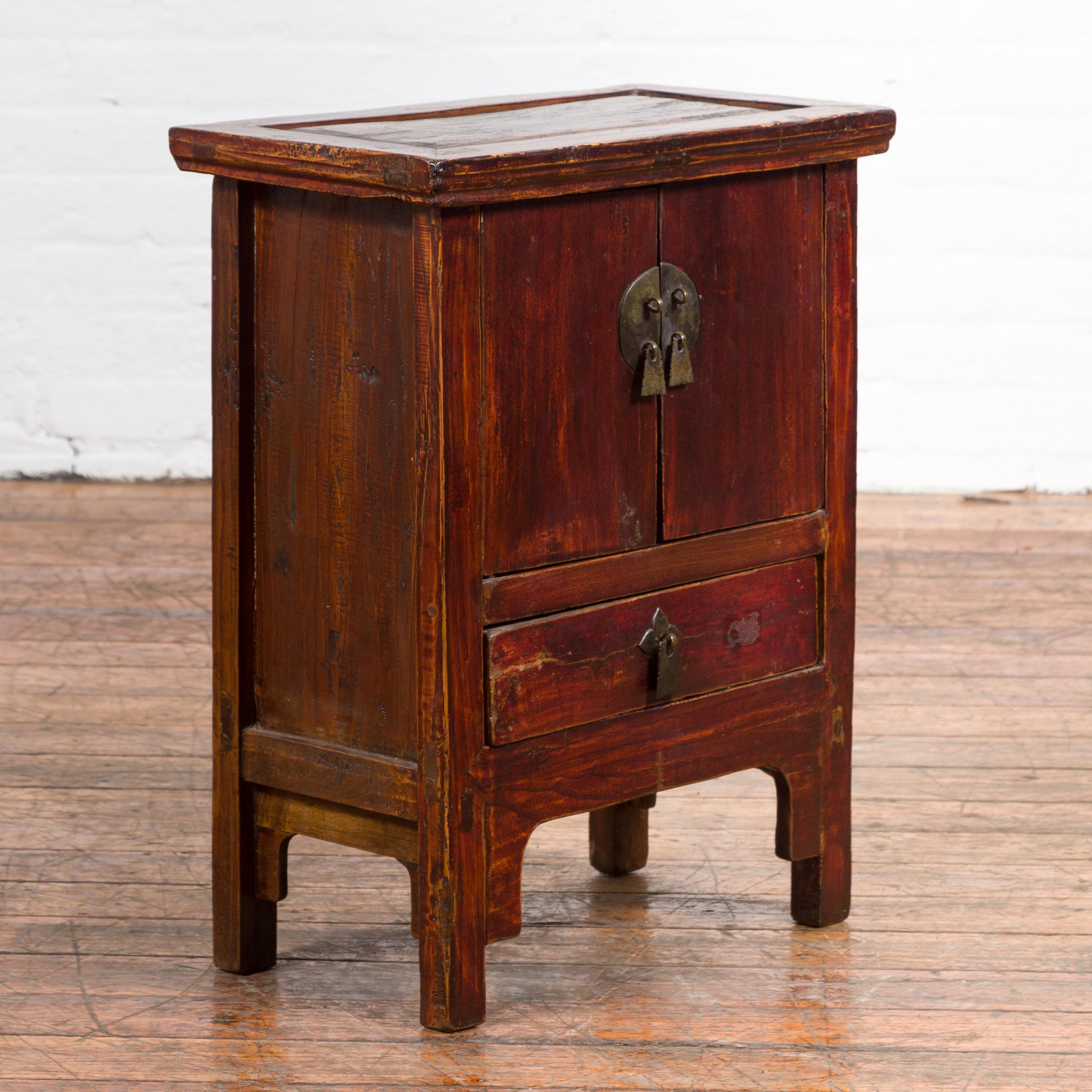 A Chinese Qing Dynasty period bedside table from the 19th century, with double doors and low drawer. Created in China during the Qing Dynasty, this bedside table features a rectangular top with central board overhanging a façade made of two doors