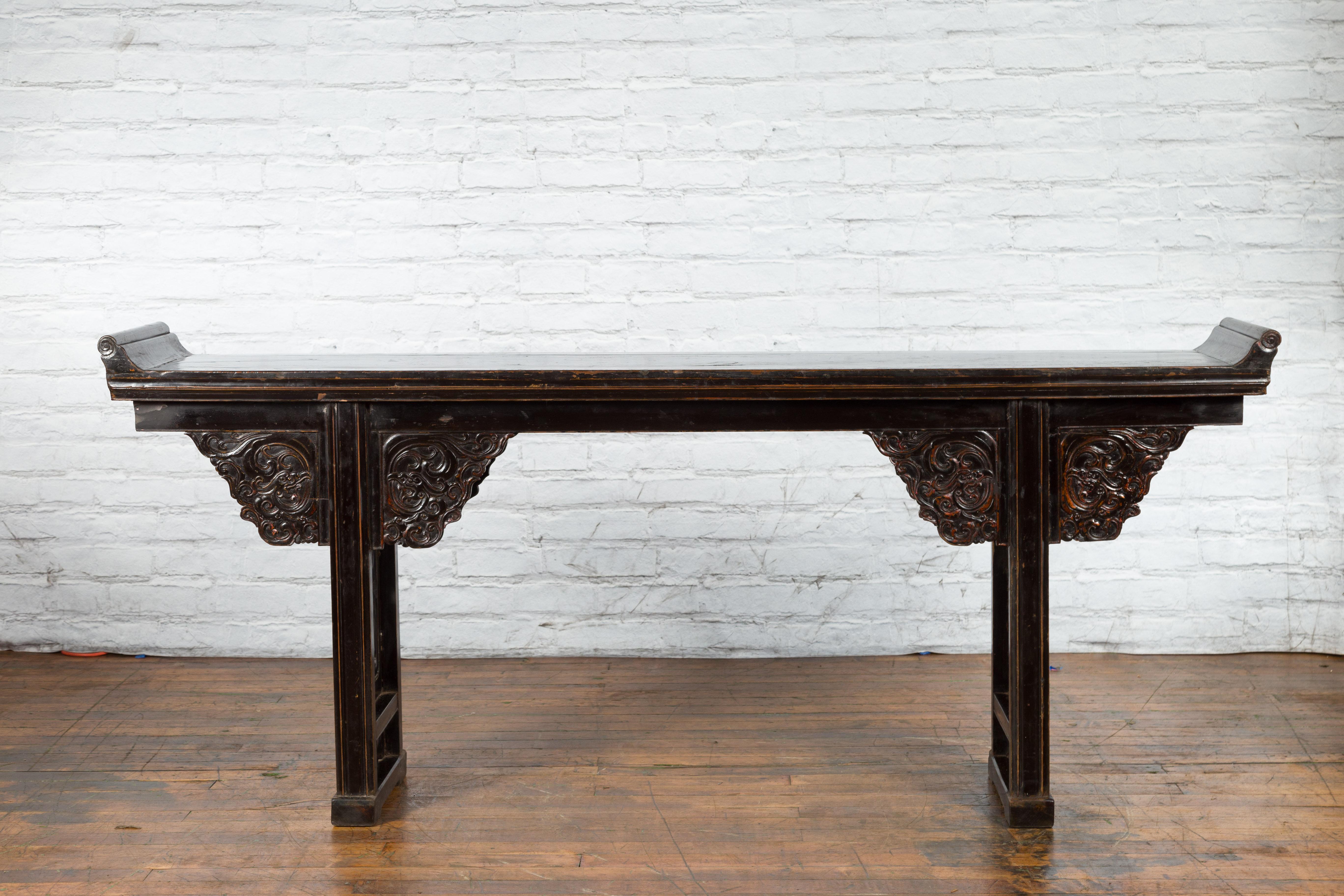 A Chinese Qing Dynasty period black lacquer altar console table from the early 19th century, with everted flanges, carved spandrels and openwork sides. Created in China during the Qing Dynasty in the early years of the 19th century, this console
