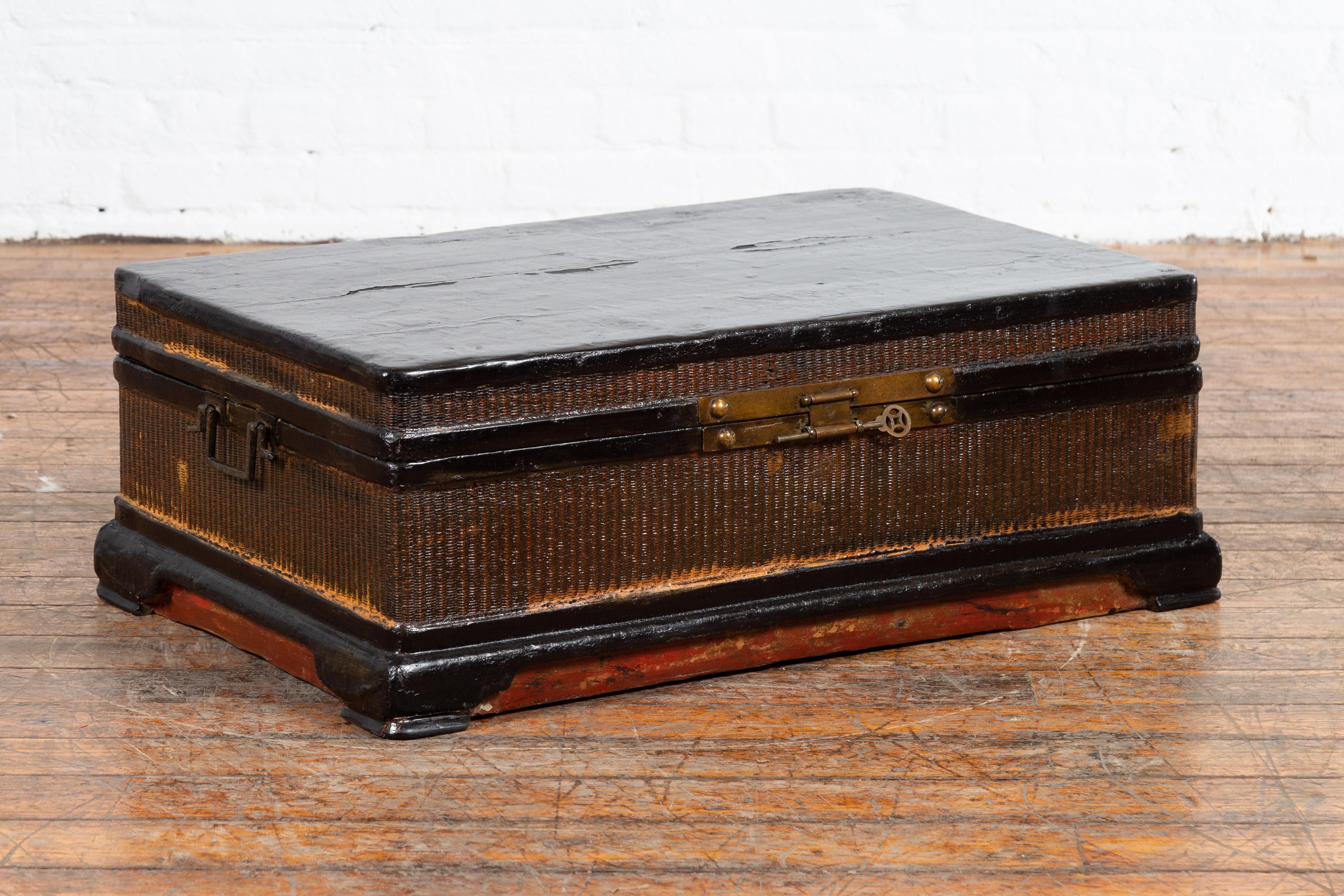 A Chinese Qing Dynasty period antique blanket chest from the 19th century, with rattan inlay. Created in China during the 19th century, this unusual blanket chest features a black lacquered top opening thanks to a brass lock with key to reveal an