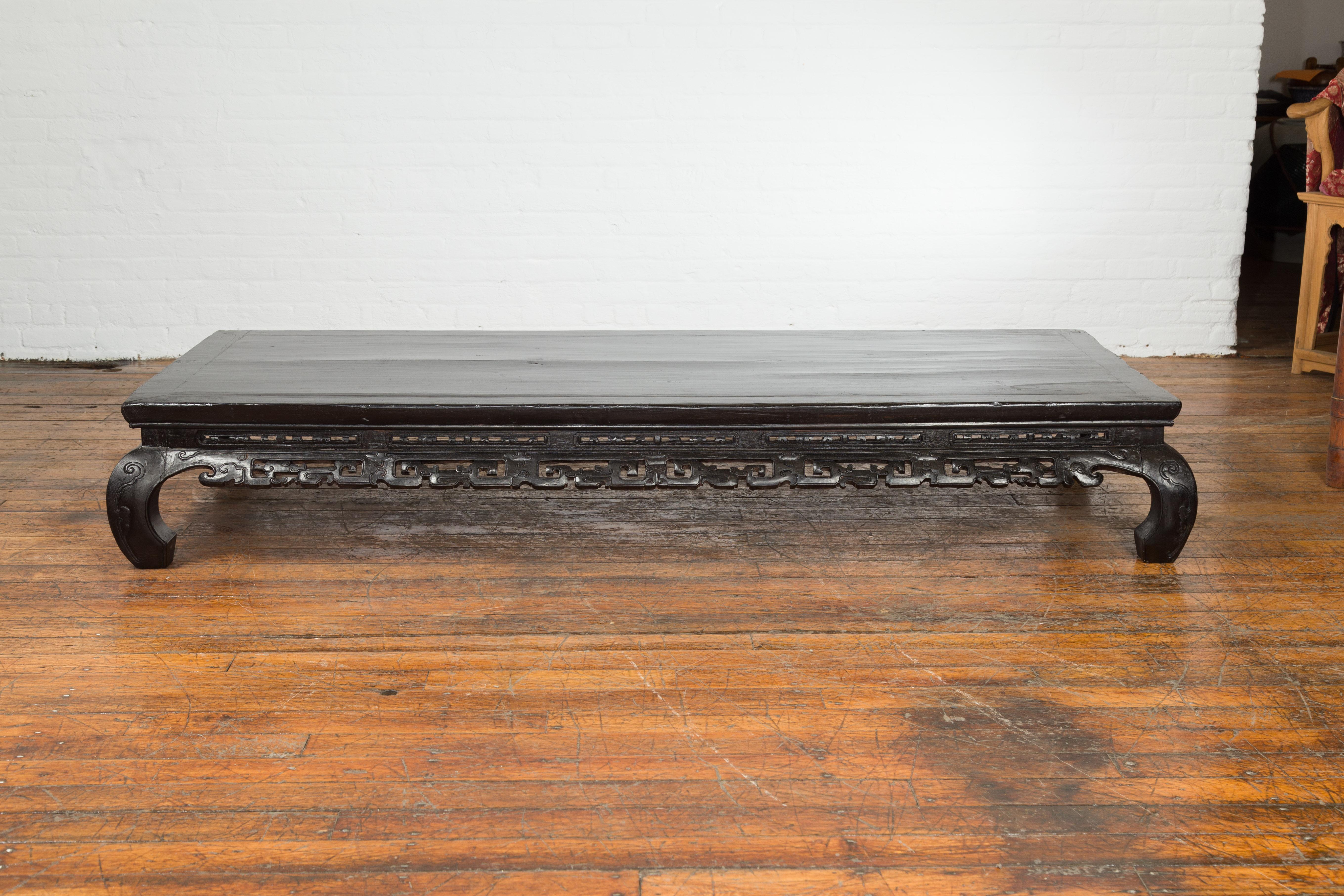 A Chinese antique Qing Dynasty period low kang black lacquer coffee table from the 19th century, with carved apron and chow legs. Created in China during the 19th century, this Qing Dynasty coffee table features a rectangular top with central board,
