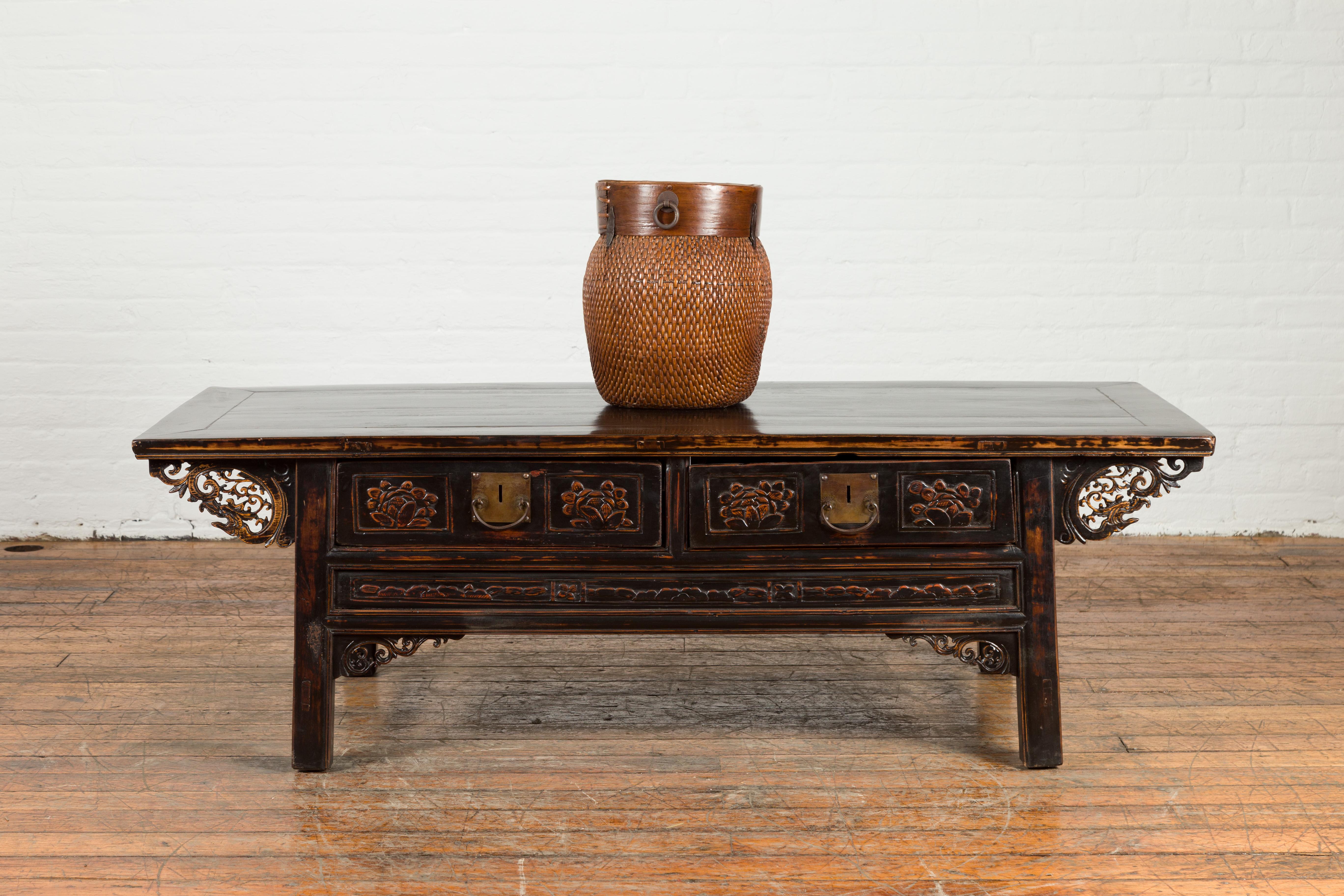 A Chinese Qing Dynasty antique black lacquer coffee table from the 19th century, with two drawers, dragon-carved spandrels and raised motifs. Created in China during the Qing Dynasty, this coffee table features a rectangular top with central board,
