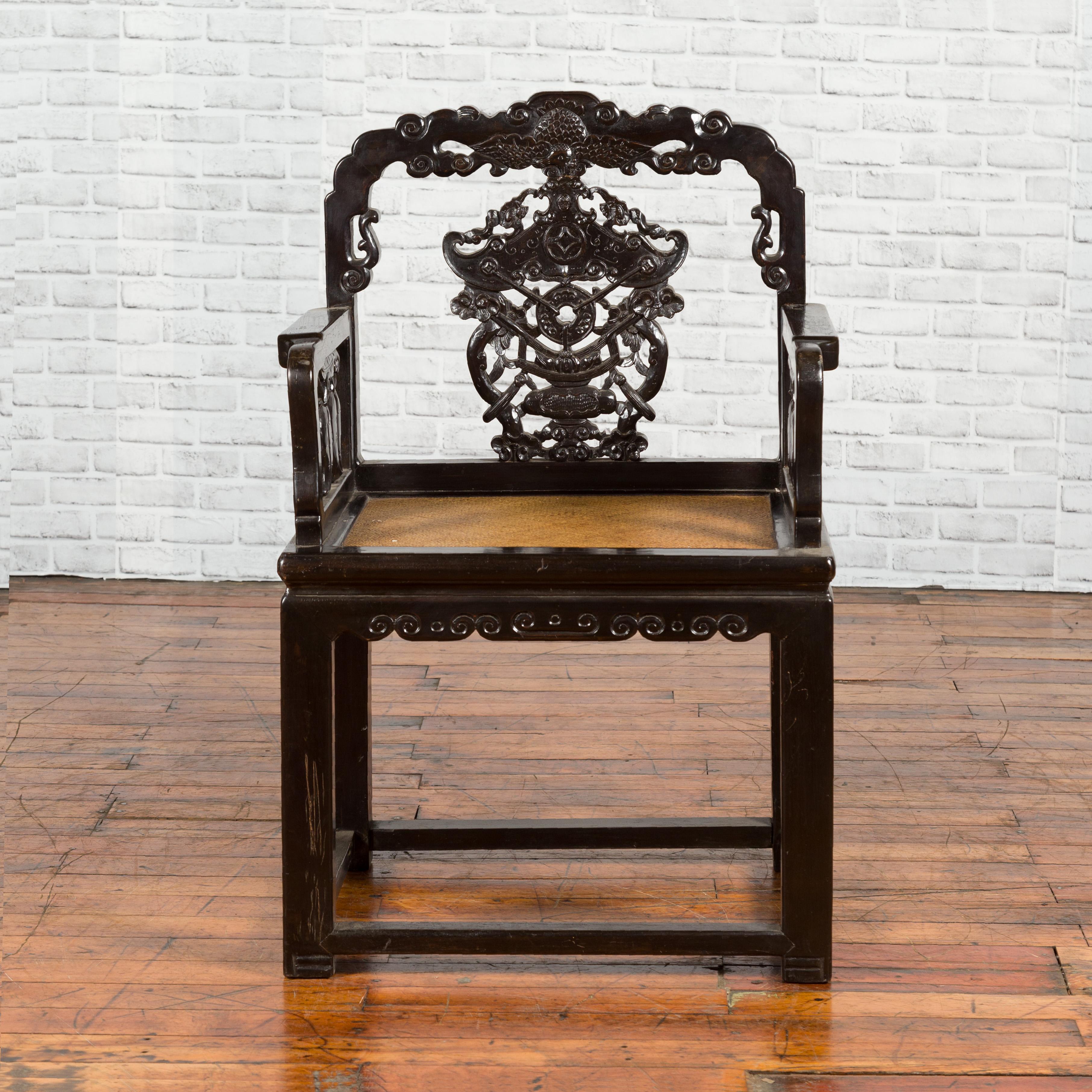 A Chinese Qing dynasty period black lacquered chair from the 19th century, with hand carved back splat and rattan seat. Created in China during the 19th century, this black lacquered armchair captures our attention with its exquisite back, adorned