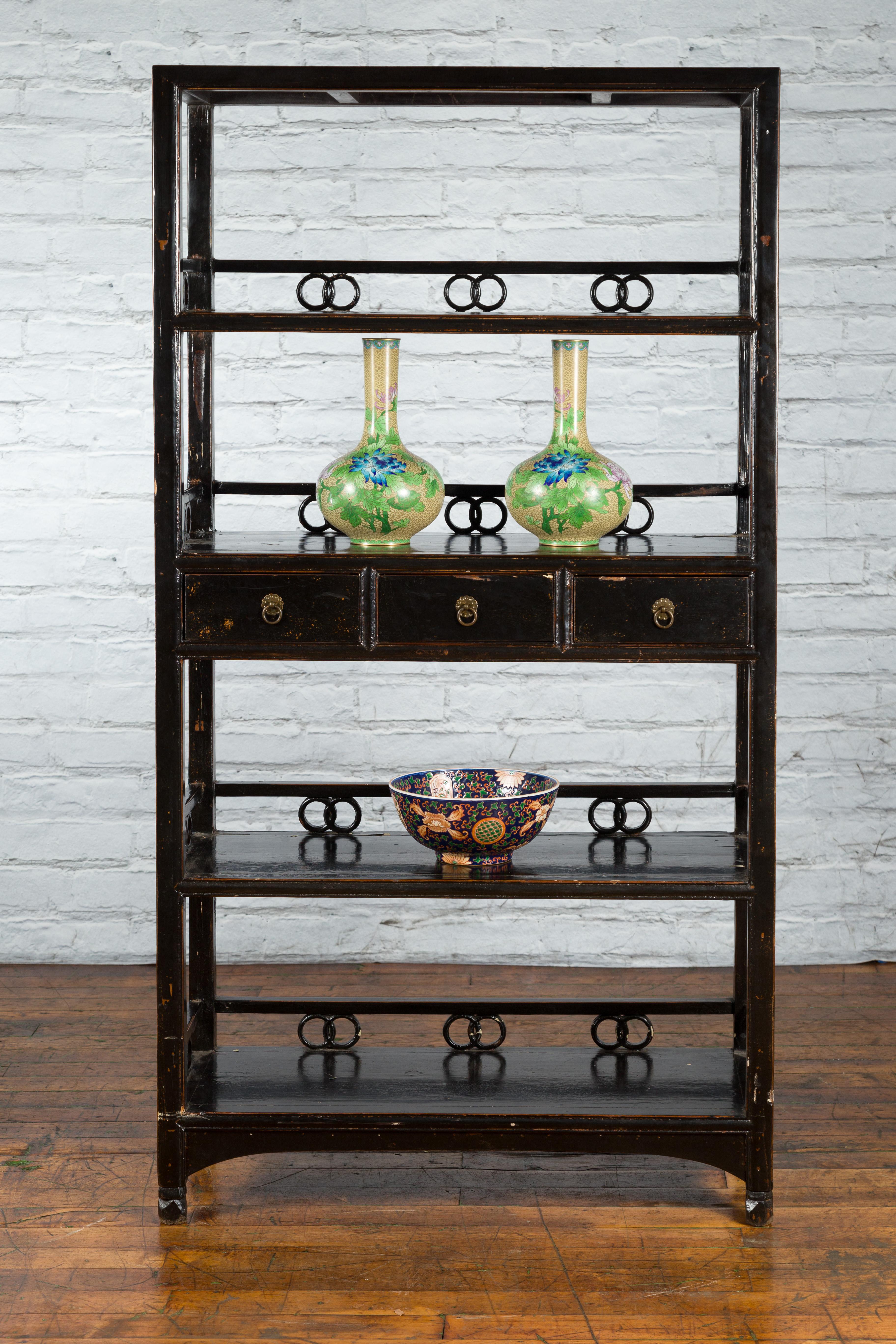 A tall Qing Dynasty period Chinese bookcase from the 19th century, with three drawers, intertwined rings and dark brown / black patina. Created in China during the Qing Dynasty, this tall bookcase features a linear silhouette contrasted by a perfect