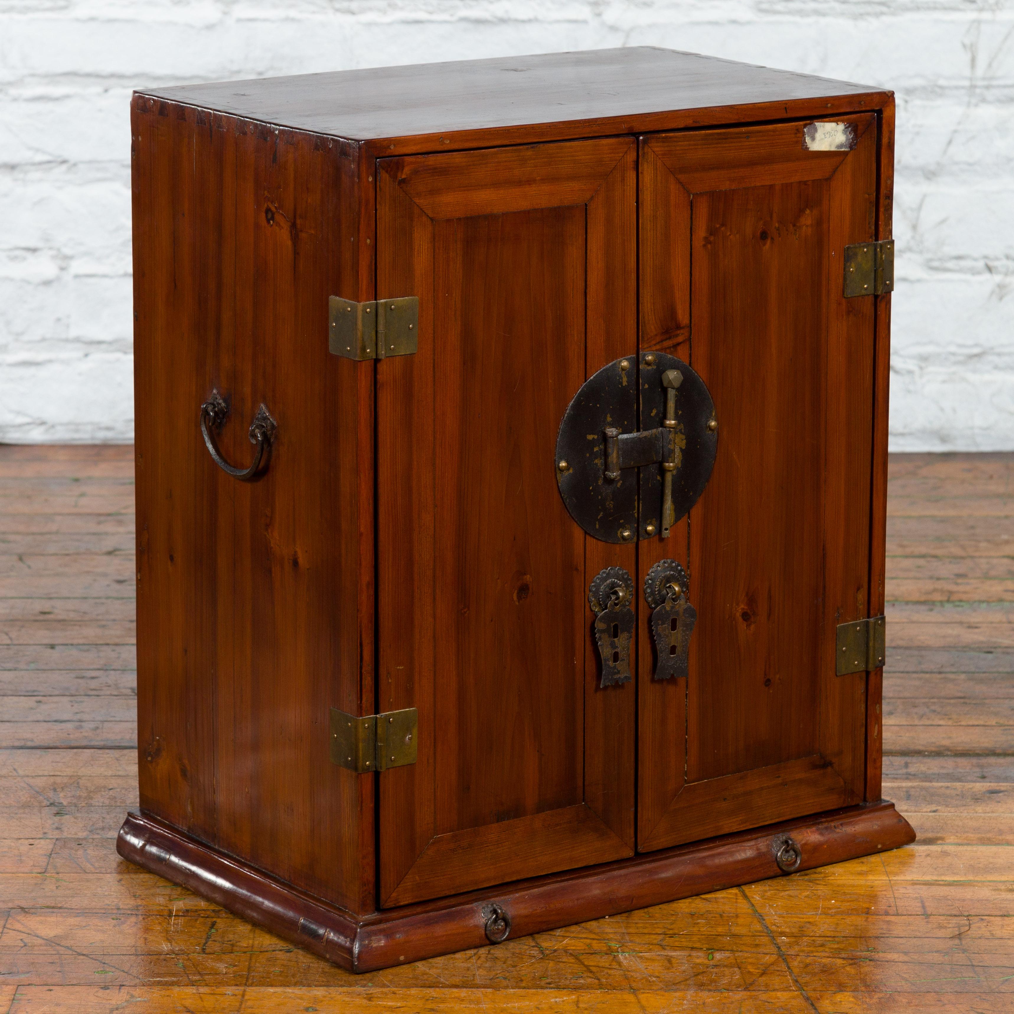 A Chinese Qing Dynasty period elm wood side cabinet from the 19th century, with two doors, bronze hardware, inner shelves and hidden drawers. Created in China during the Qing Dynasty period in the 19th century, this elm wood side cabinet features a