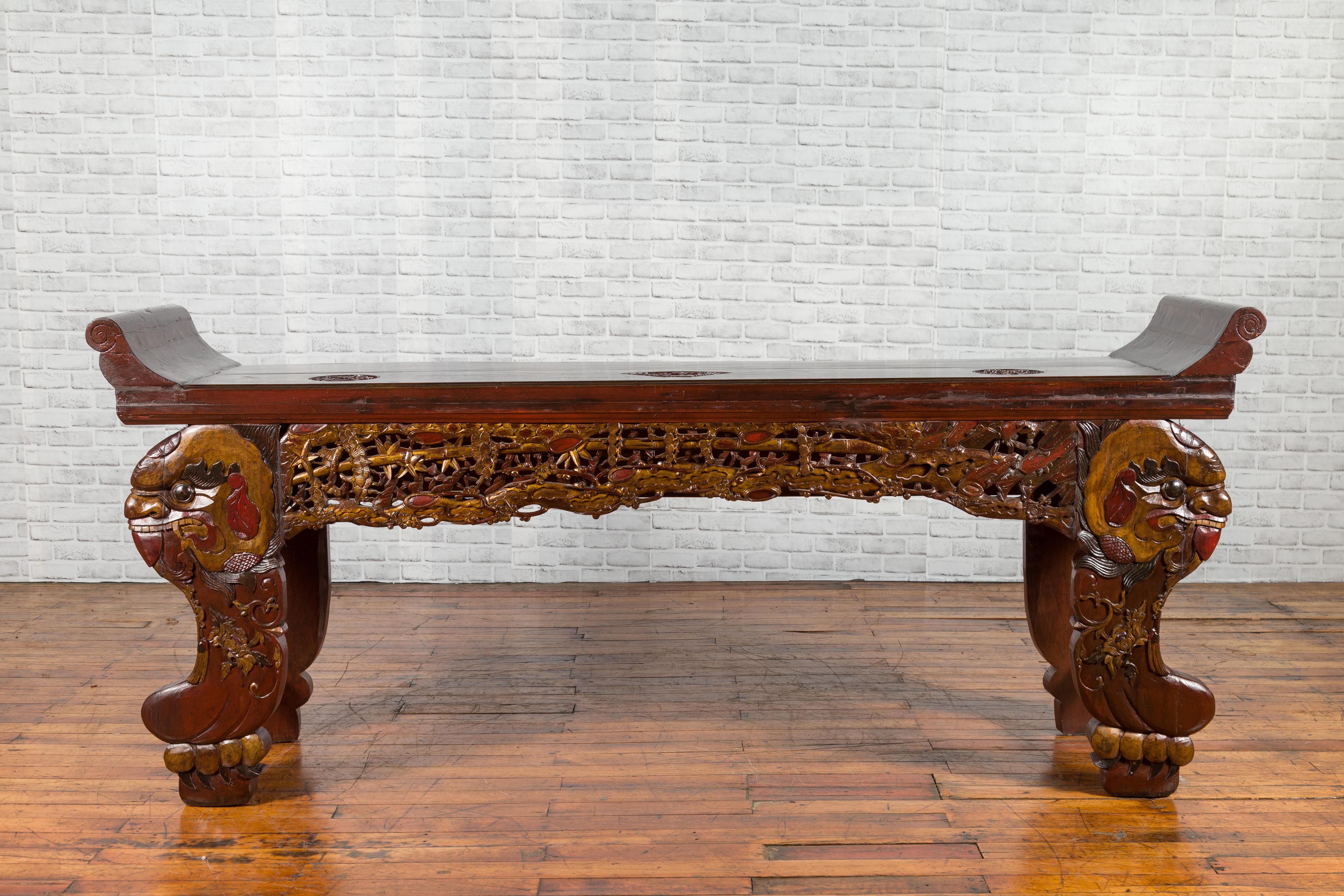 A Chinese antique Qing Dynasty carved altar console table from the 19th century, with everted flanges, mythical animals, dark reddish / brown finish and gilt accents. Created in China during the 19th century, this altar console table features a