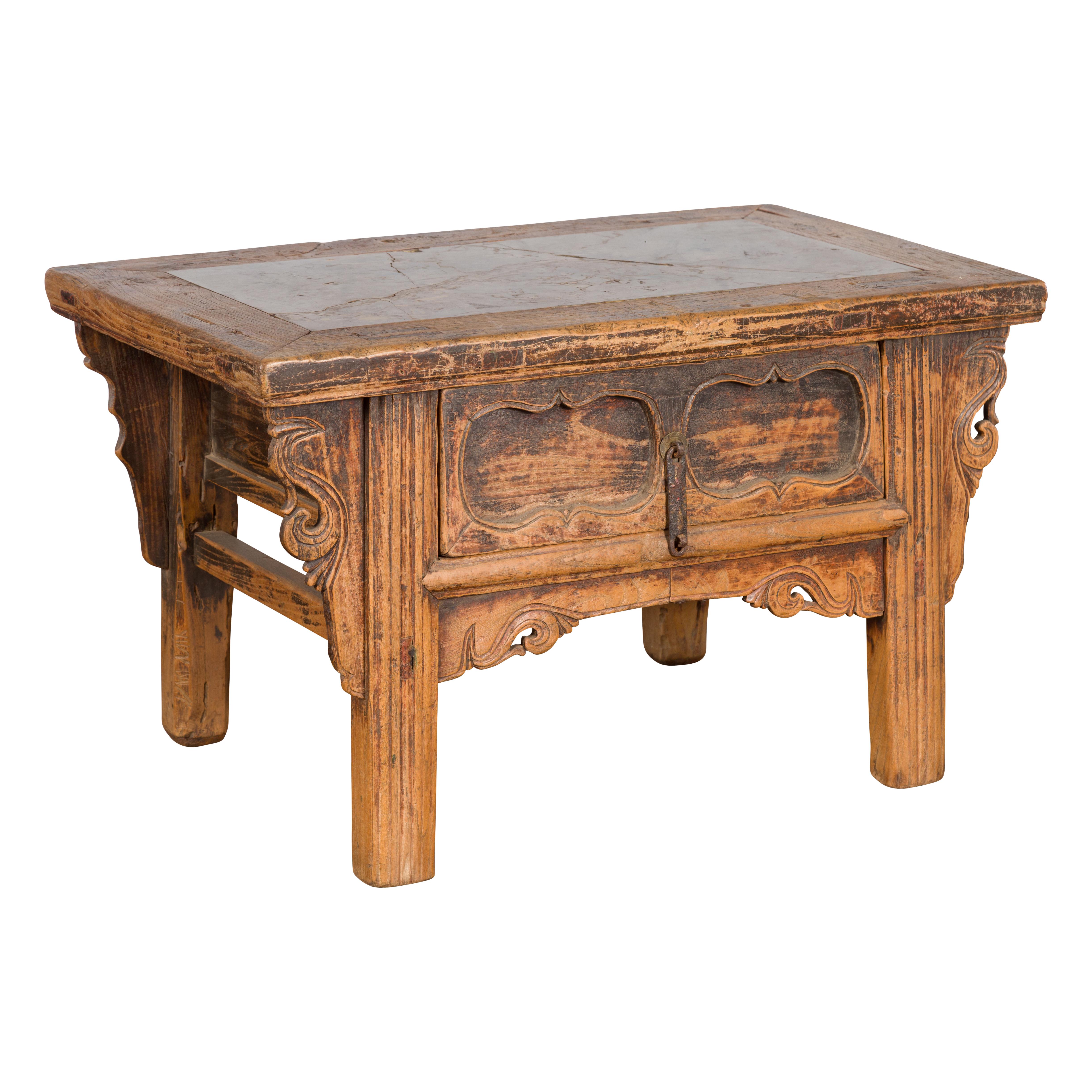 A Chinese Qing Dynasty low elm table from the 19th century, with Ming stone inset, carved spandrels and recessed cartouches. Created in China during the Qing Dynasty period, this elm table features a rectangular top with Ming stone inset, sitting
