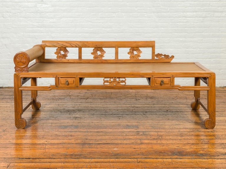 A Chinese Qing Dynasty period opium bed from the 19th century with rattan inset, removable arm, drawers and carvings. Born in China during the 19th century, this opium daybed features a removable pierced back adorned with carved clouds, connected on