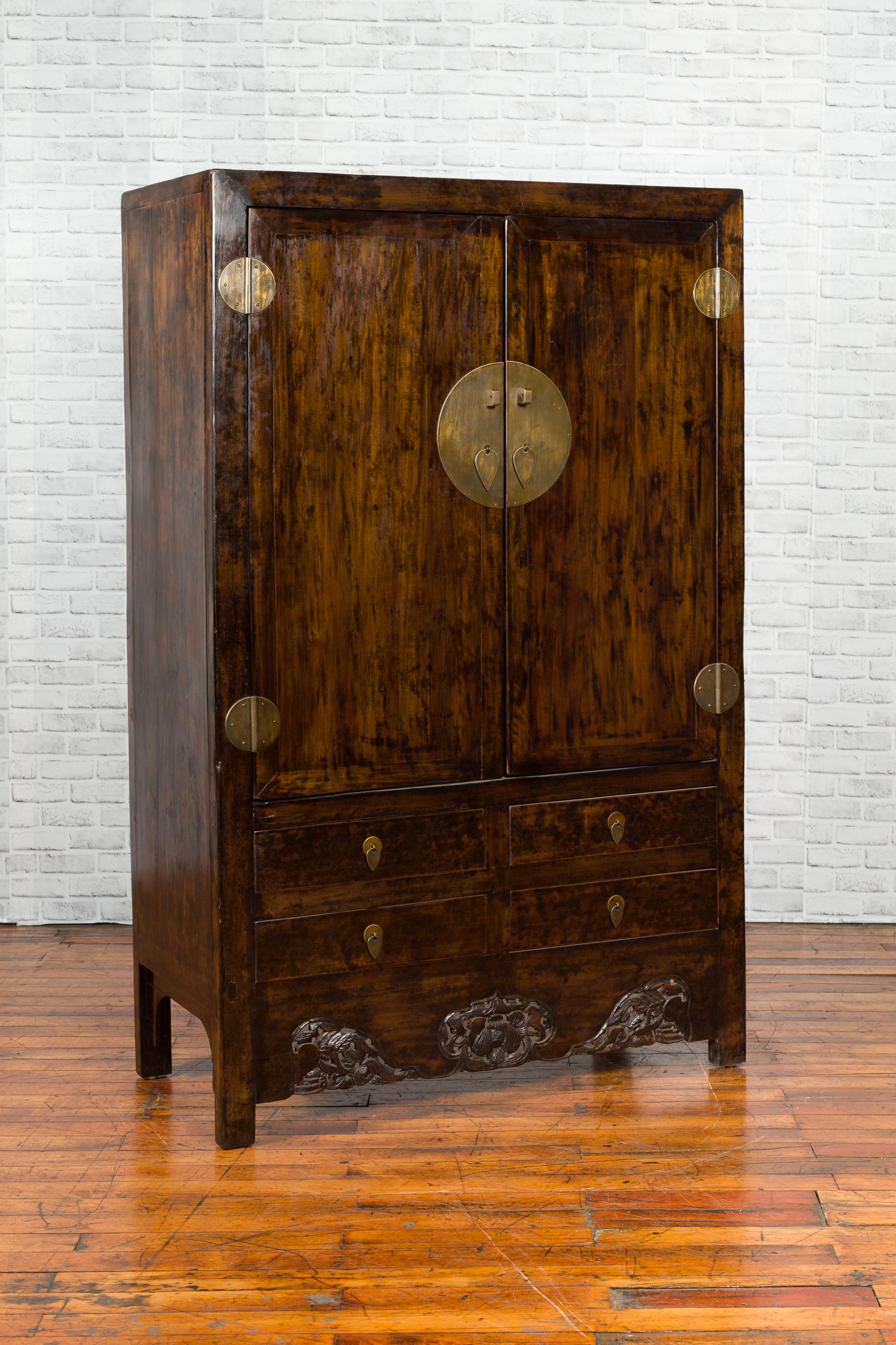 A Chinese Qing dynasty period elm cabinet from the 19th century, with two doors, four drawers and carved apron. Created in China during the Qing dynasty, this elm cabinet captures our attention with its dark brown patina perfectly contrasted by the