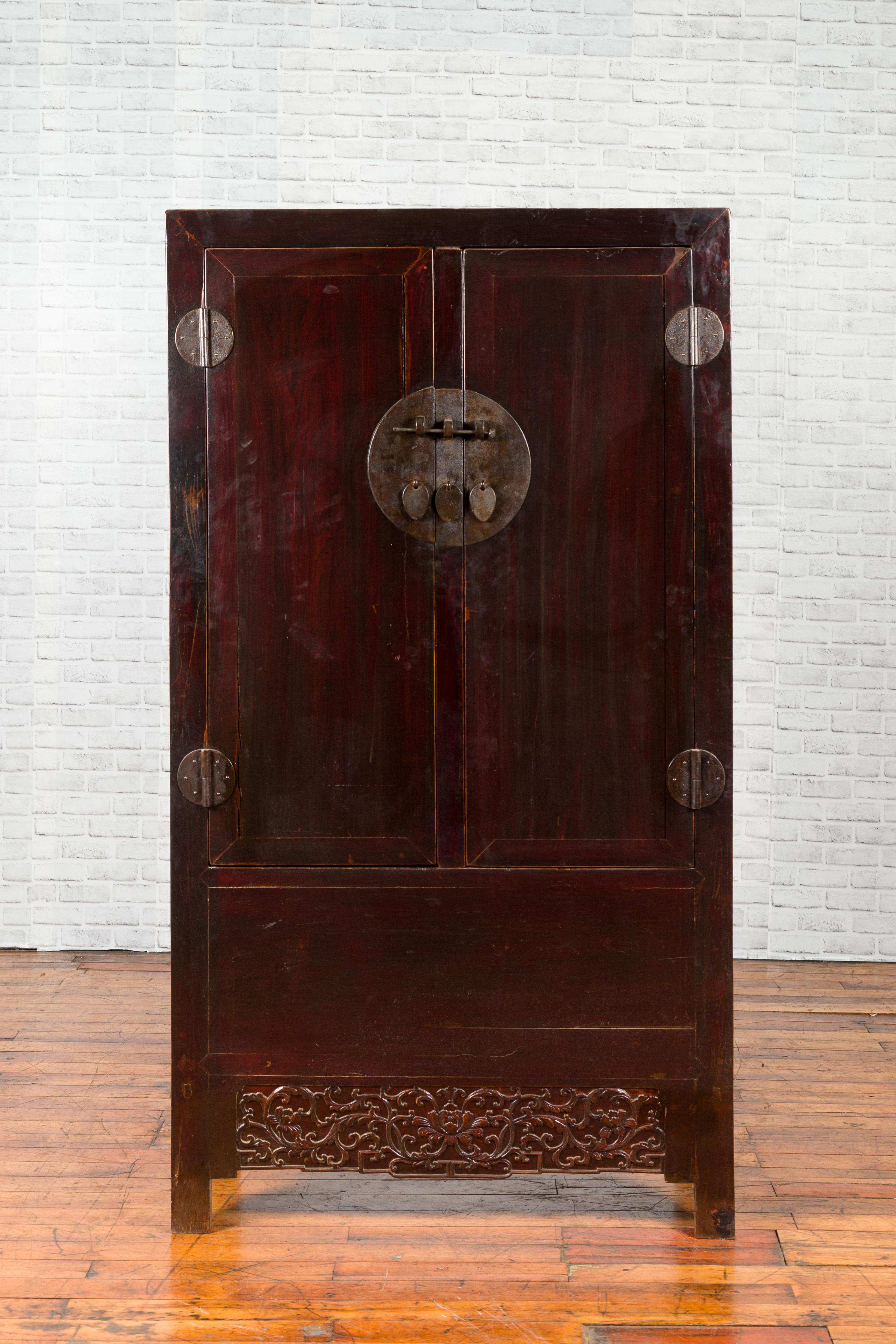 A Chinese Qing dynasty period dark brown lacquered cabinet from the 19th century, with carved scrolling foliage and medallion hardware. Created in China during the Qing dynasty, this cabinet features a linear silhouette perfectly complimenting the