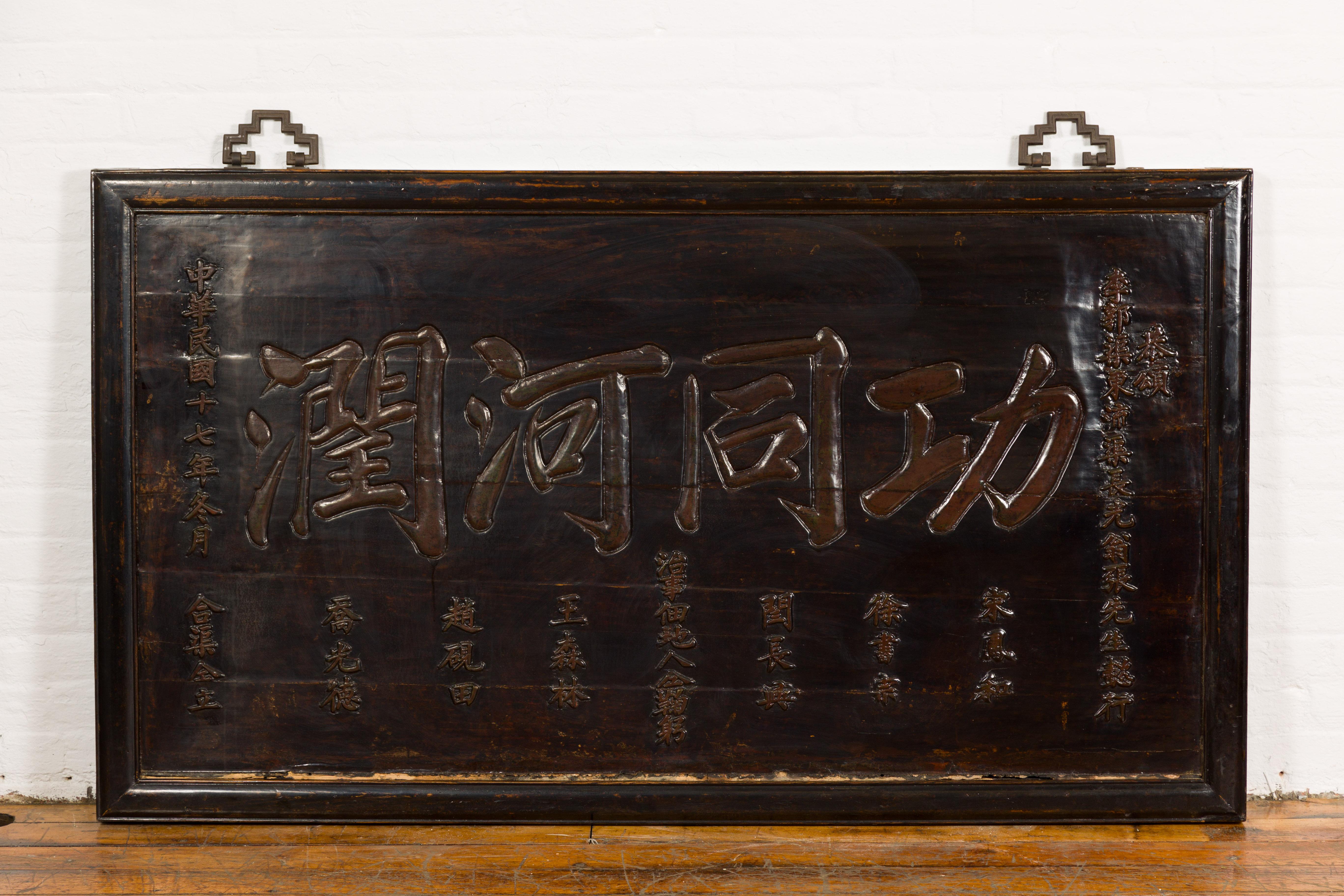 A Chinese Antique Shop Sign with Carved Calligraphy from the 19th century with dark brown/black lacquer, calligraphy carved in low relief and iron hardware. Immerse yourself in the rich tapestry of Chinese history with this authentic 19th-century