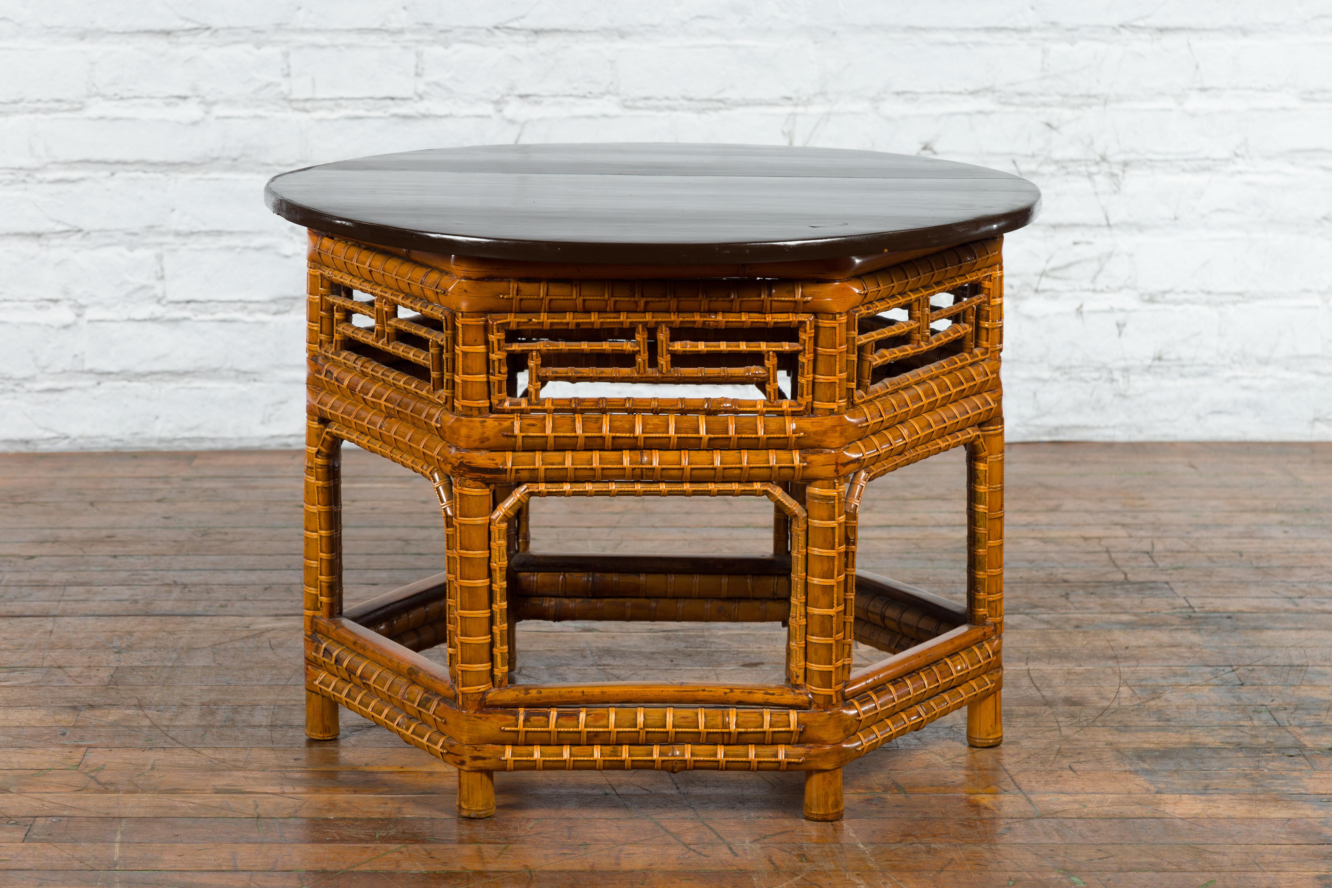 A Chinese Qing Dynasty period coffee table from the 19th century, with black lacquered elm wood top, hexagonal bamboo base and fretwork design. Created in China during the Qing Dynasty in the 19th century, this coffee table features a circular elm