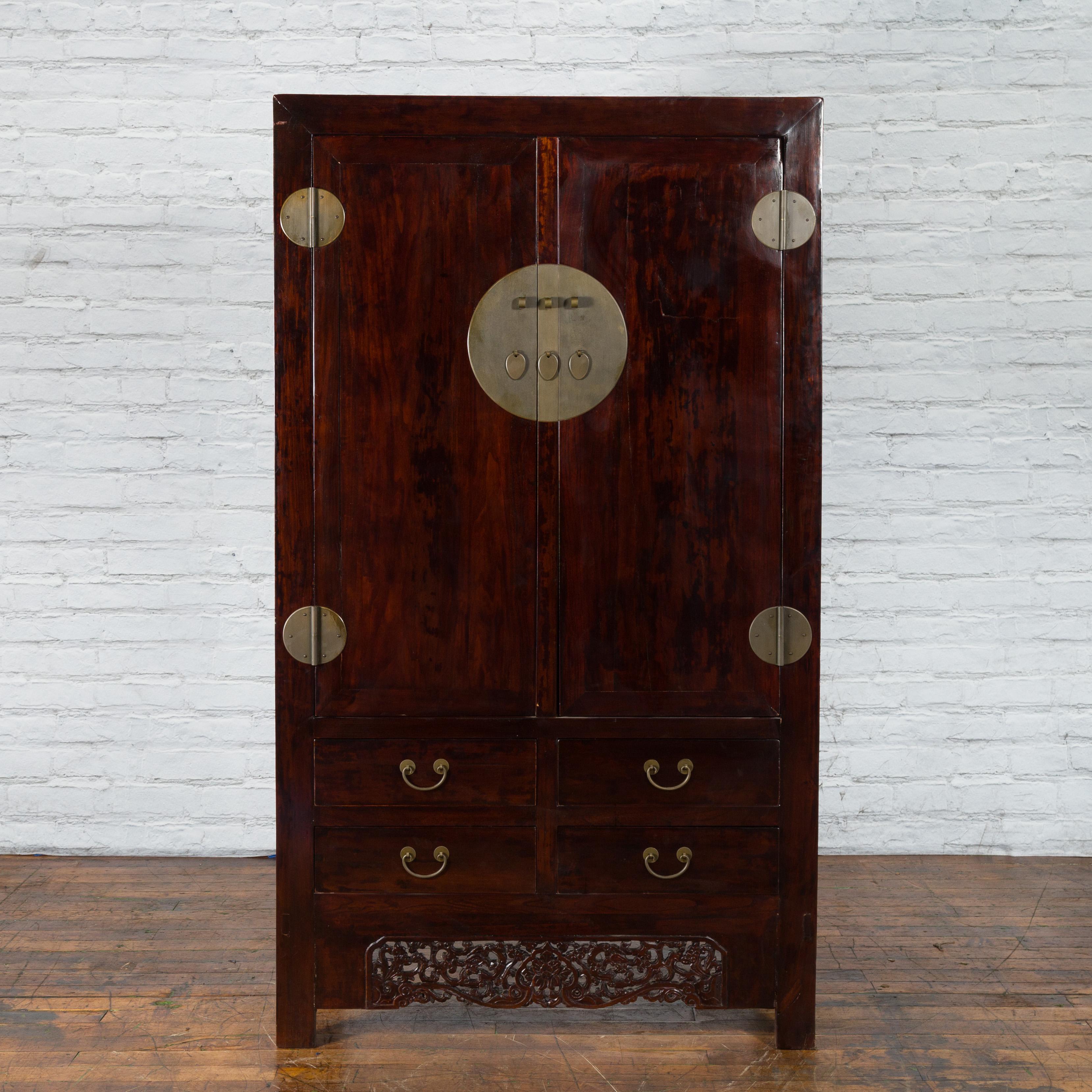 A Chinese Qing Dynasty period elm wood cabinet from the 19th century with double doors, four drawers, large brass medallion hardware and carved apron. We currently have two cabinets available, priced and sold individually. Created in China during