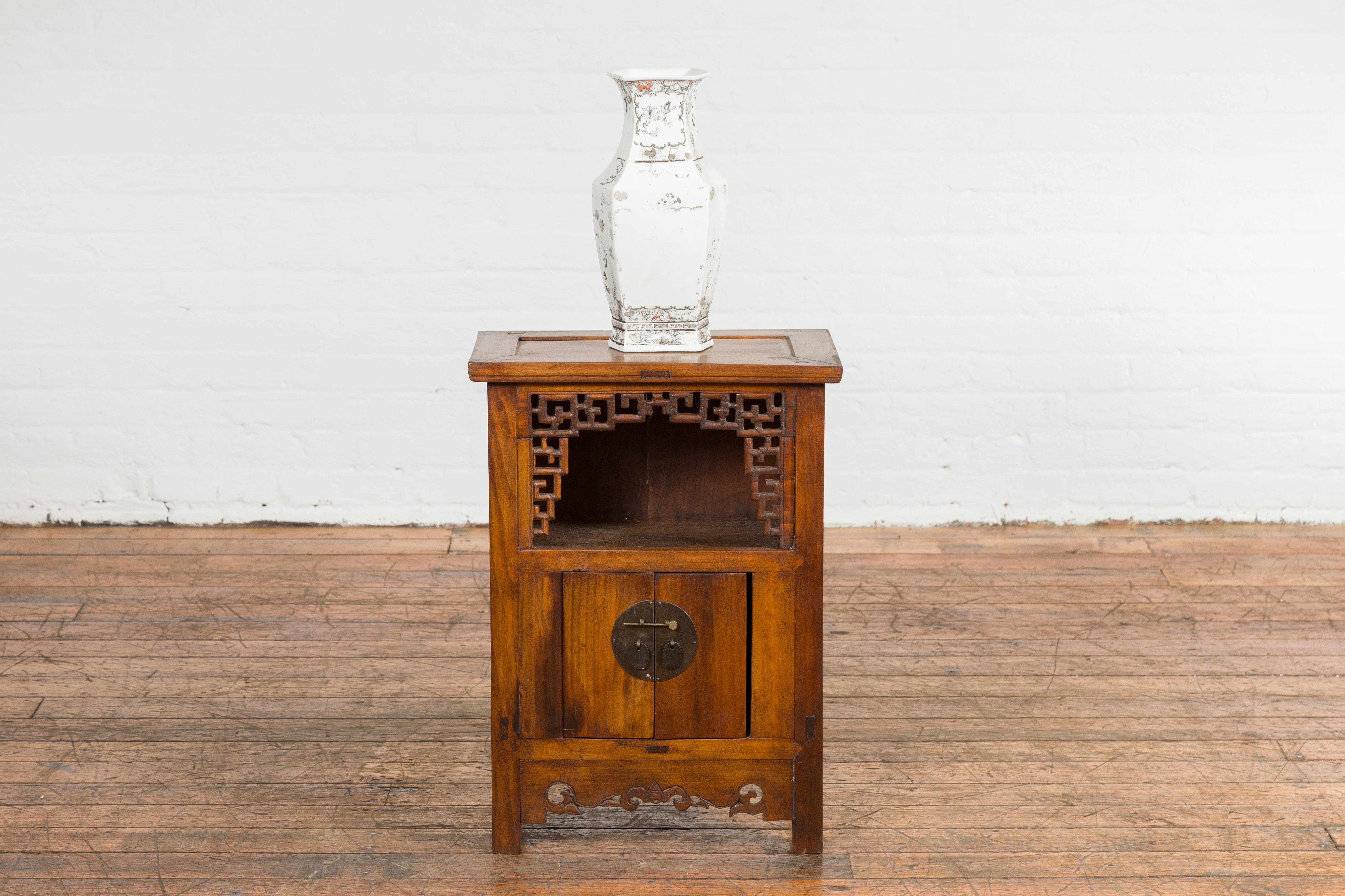 A Chinese Qing Dynasty period brown elm wood side cabinet from the 19th century with fretwork motifs, open shelf and double doors. Created in China during the Qing Dynasty period in the 19th century, this elm wood side cabinet features a warm brown