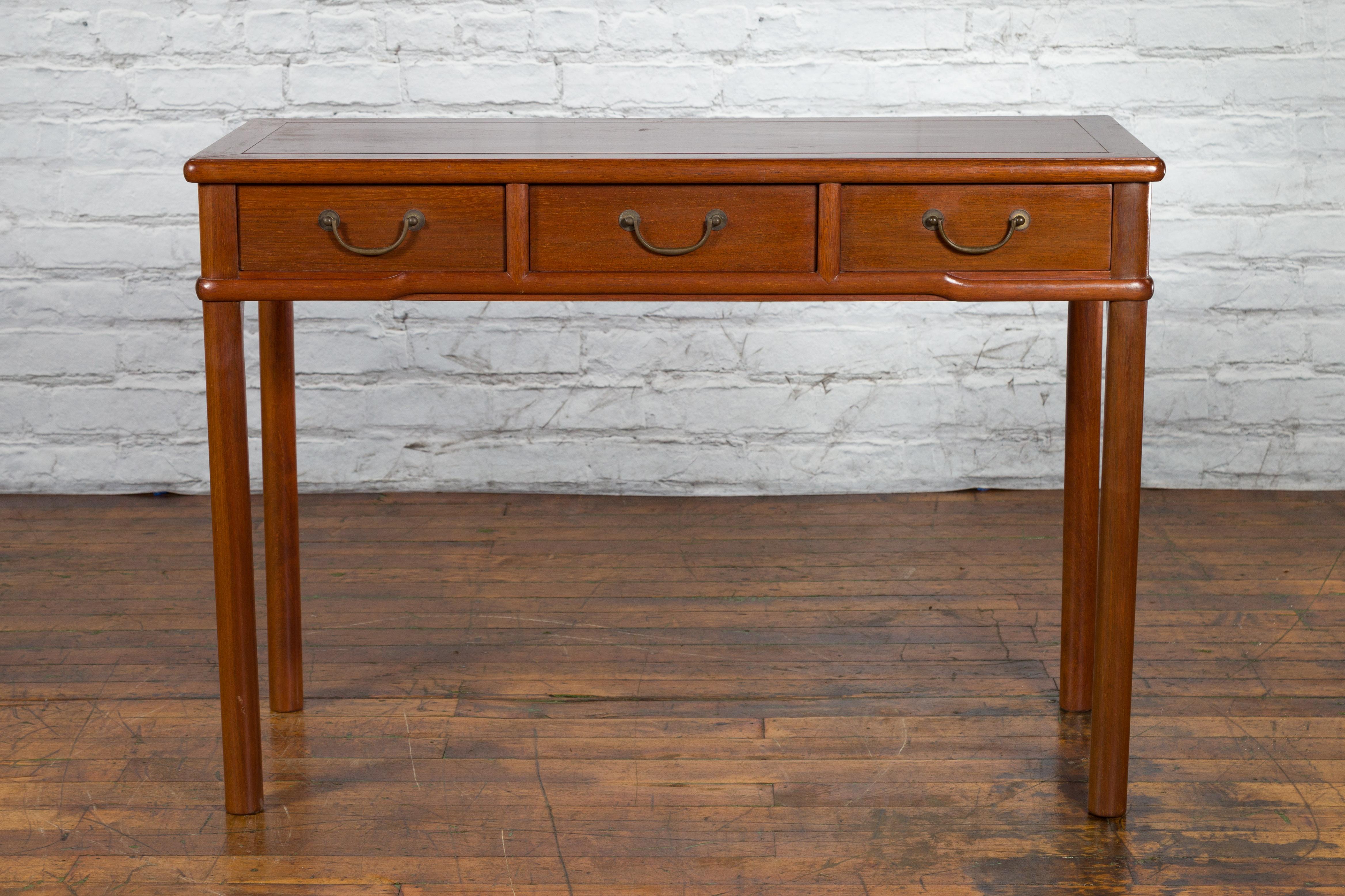 A Chinese Qing Dynasty period elm wood desk from the 19th century with three drawers and bail handles. Created in China during the Qing Dynasty, this elmwood desk features a rectangular top with central board, sitting above three drawers fitted with