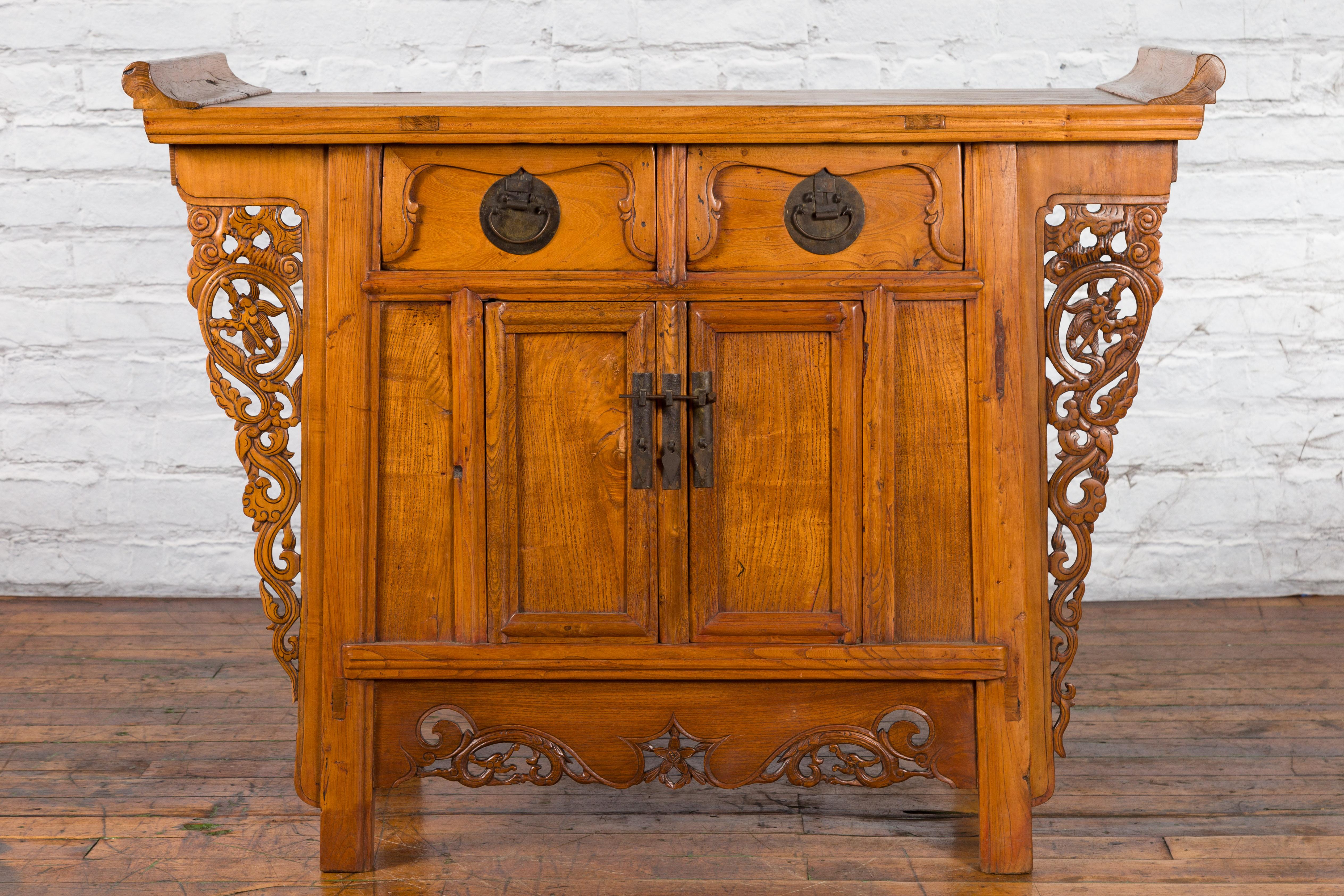 A Chinese Qing Dynasty natural elmwood altar cabinet from the 19th century, with carved spandrels and everted flanges. Created in China during the Qing Dynasty period, this natural elm cabinet features a rectangular top flanked with everted flanges,