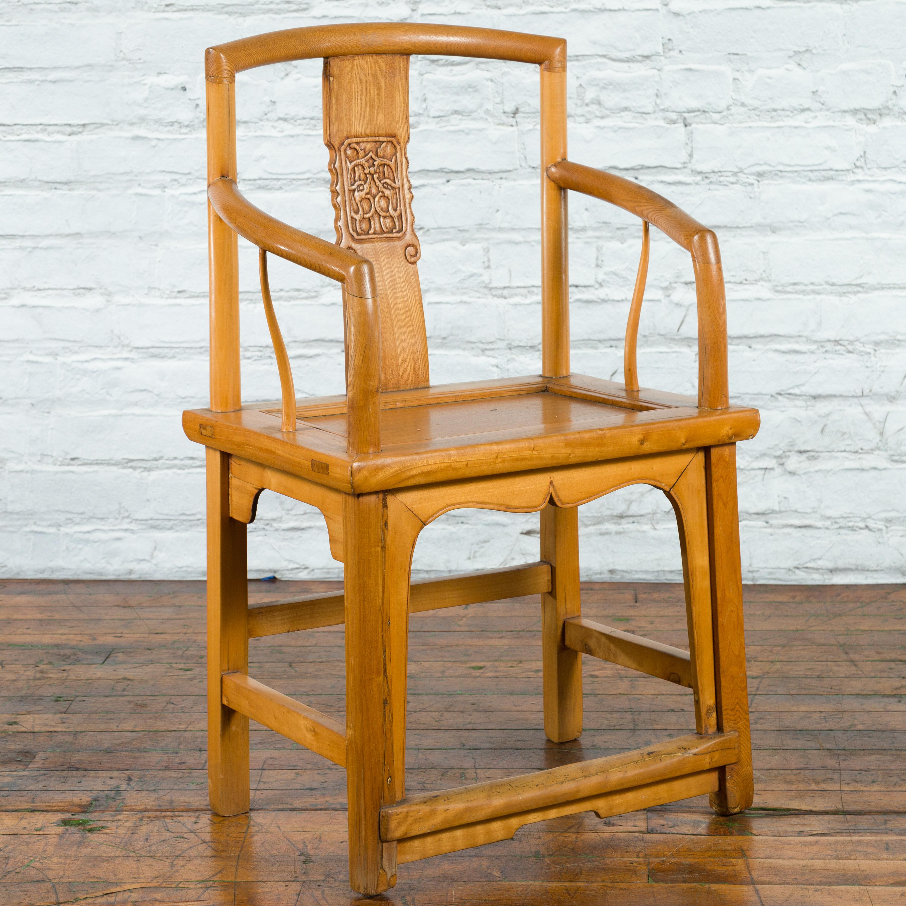 A Chinese Qing Dynasty period elm wood armchair from the 19th century, with open back, carved splat, serpentine arms, wooden seat and carved apron. Created in China during the Qing Dynasty period in the 19th century, this elm wood armchair features