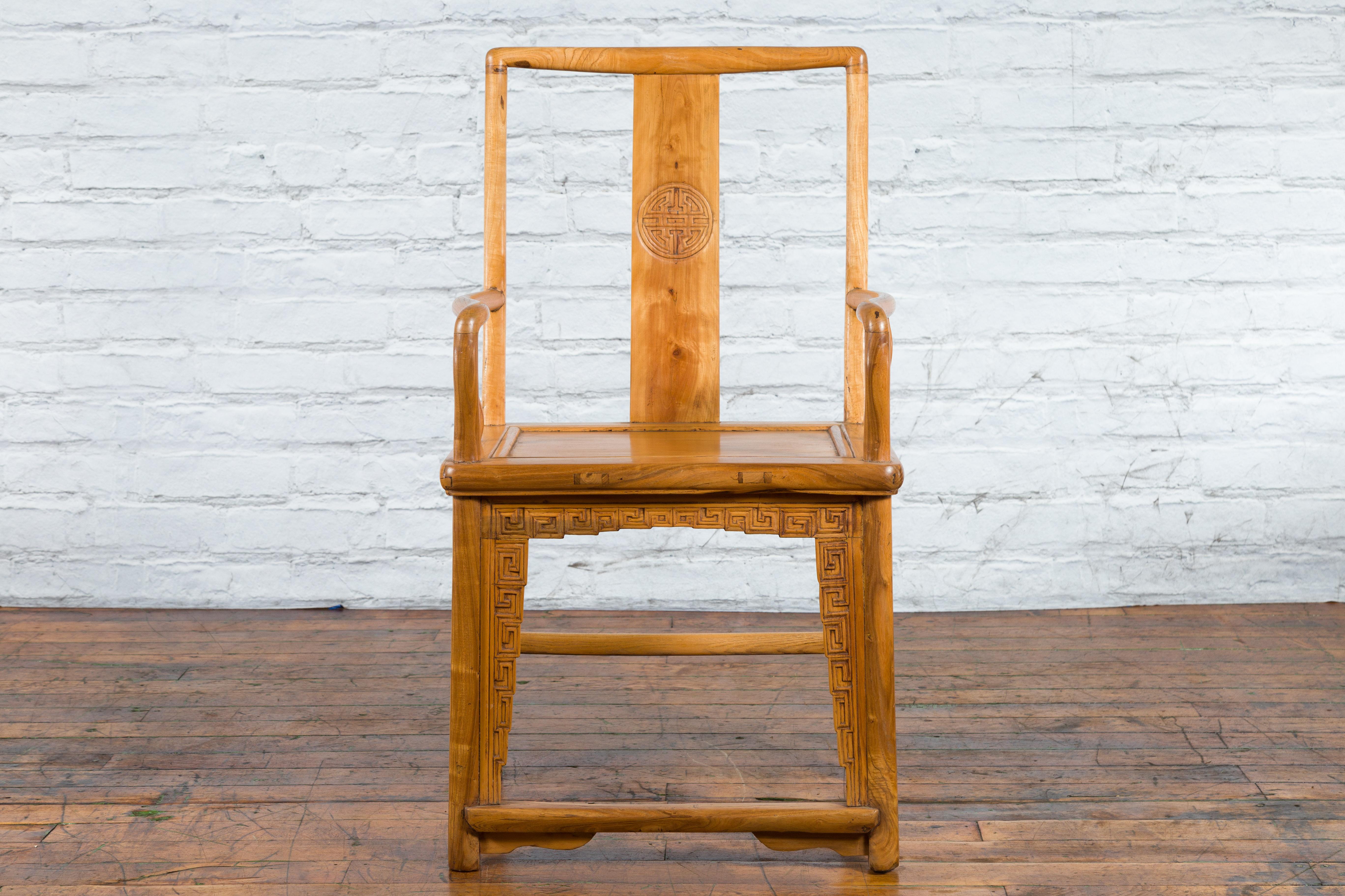 A Chinese Qing Dynasty period elm wood armchair from the 19th century, with open back, carved splat, serpentine arms, wooden seat and meander-carved apron. Created in China during the Qing Dynasty period in the 19th century, this elm wood armchair