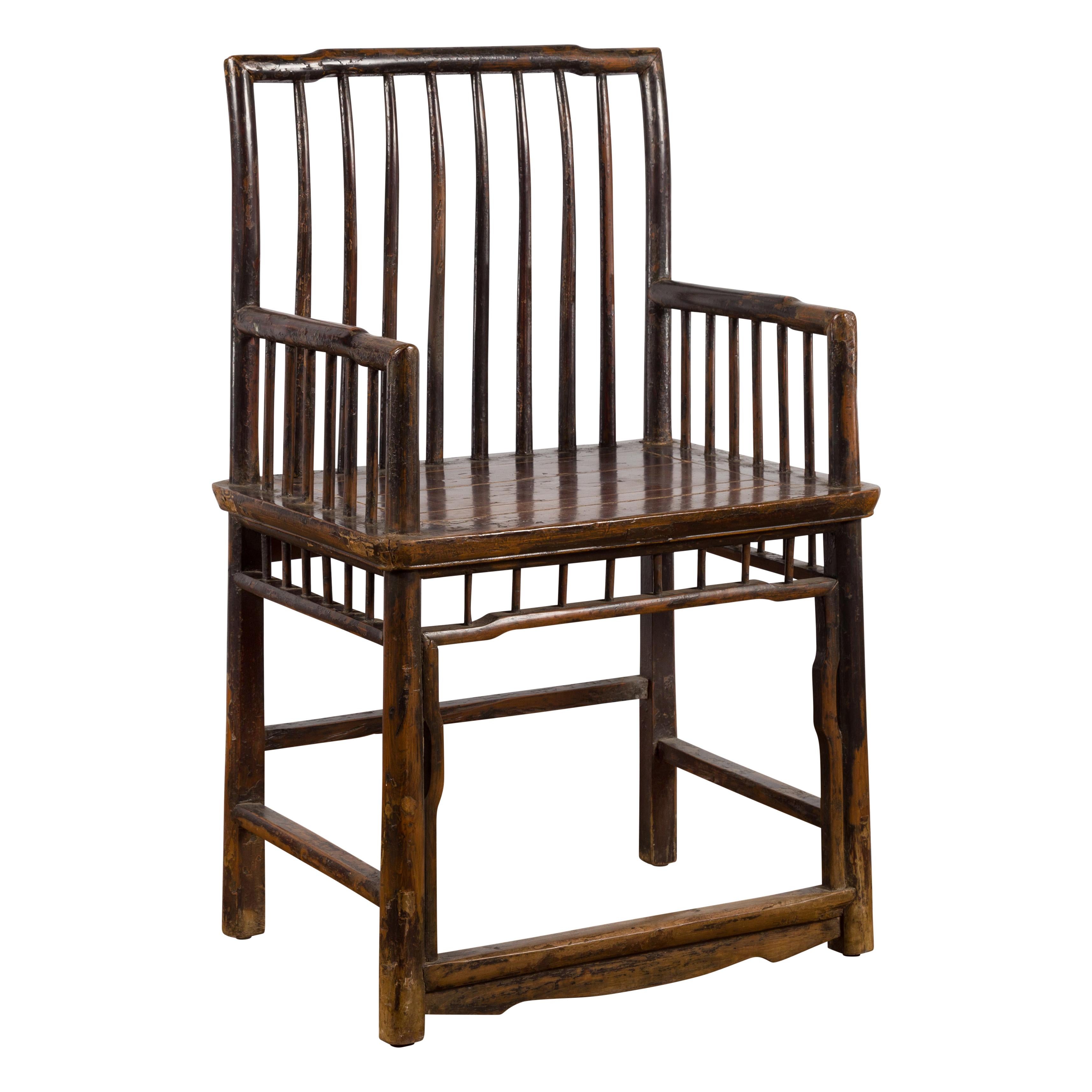 A Chinese Qing Dynasty elmwood armchair from the 19th century with slatted back and arms. Created in China during the Qing Dynasty, this elmwood chair features a pierced slatted back connected to two arms of similar style flanking a central wooden