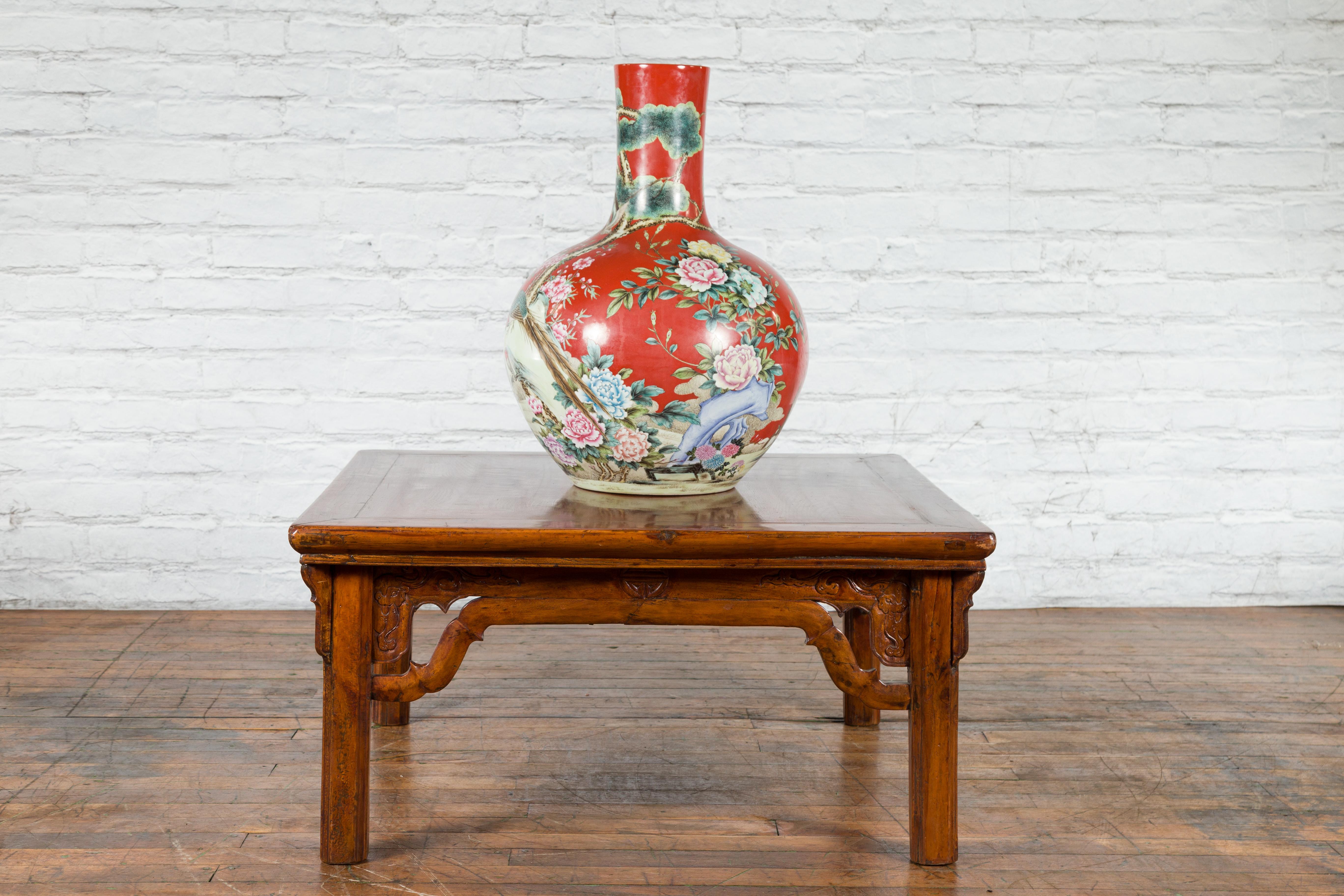 A Chinese Qing Dynasty period elm wood coffee table from the 19th century with dragon-carved apron, humpback stretchers and angled spandrels. Created in China during the Qing Dynasty period in the 19th century, this elm wood coffee table features a