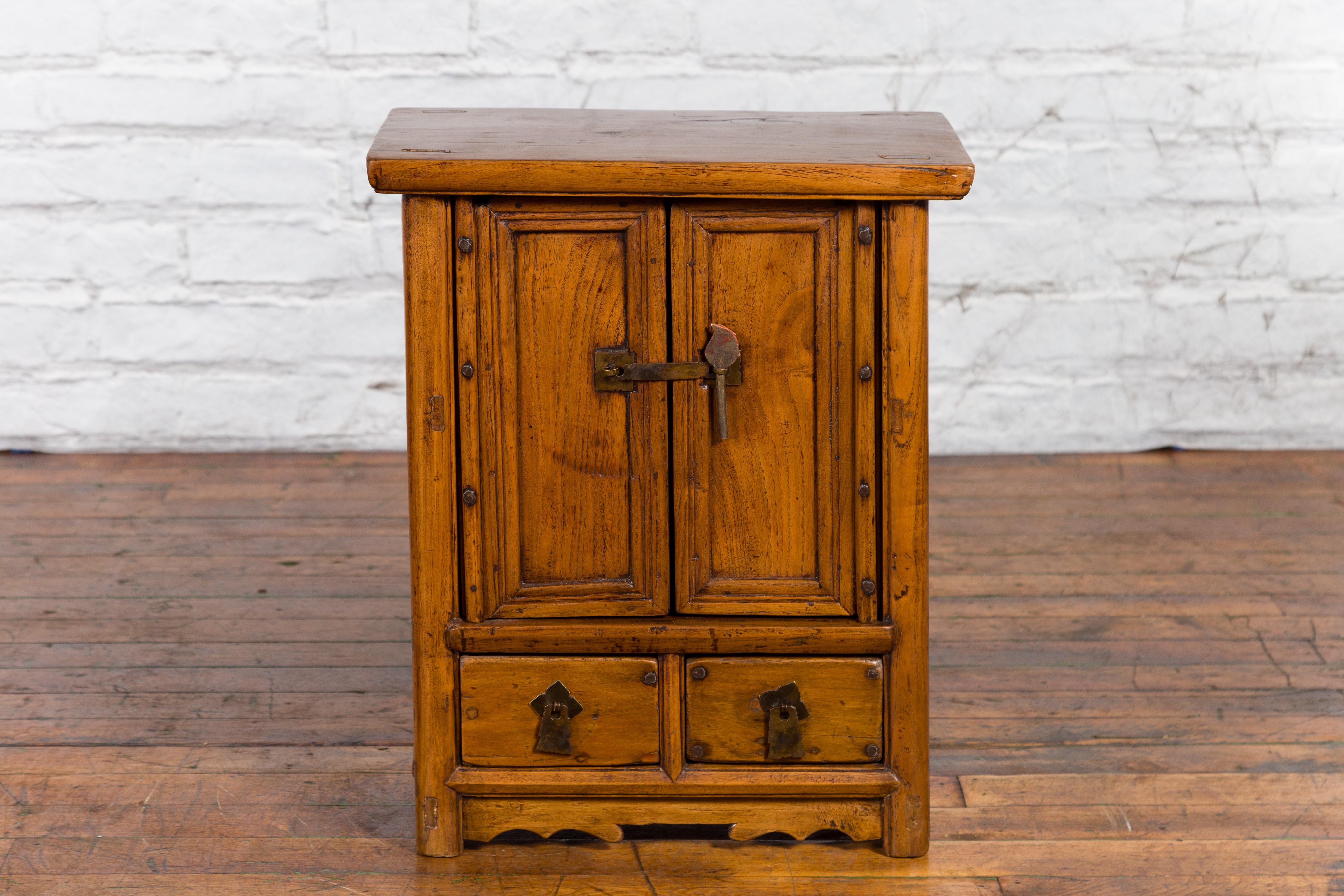 A Chinese Qing Dynasty period elmwood side cabinet from the 19th century, with double doors and two drawers. Created in China during the Qing Dynasty, this elmwood cabinet features a rectangular top sitting above two small doors fitted with a brass