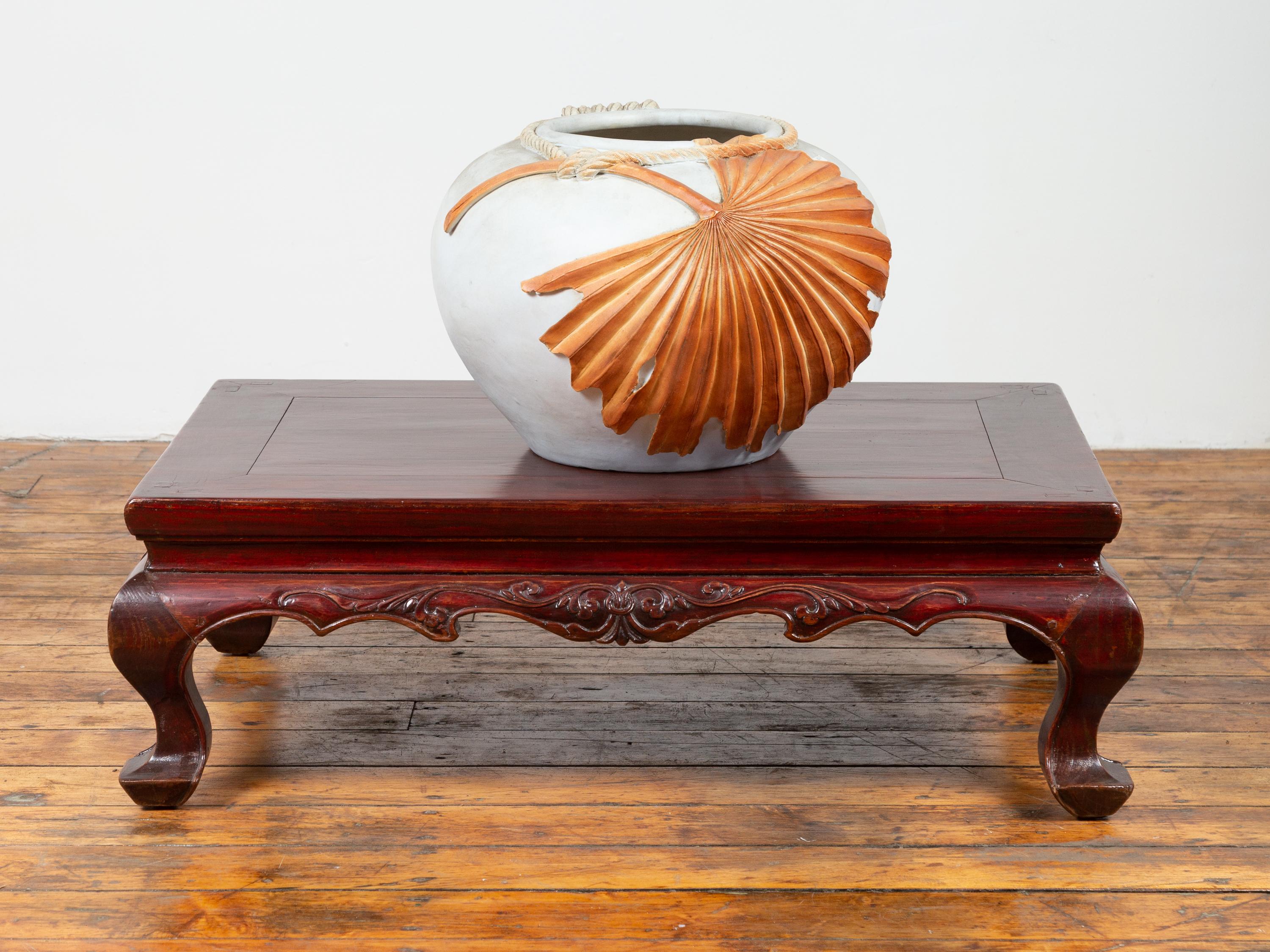 A Chinese Qing dynasty period lacquered low table from the 19th century with carved apron and cabriole legs. Born in China during the 19th century, this exquisite low table features a rectangular waisted planked top, sitting above a scalloped apron