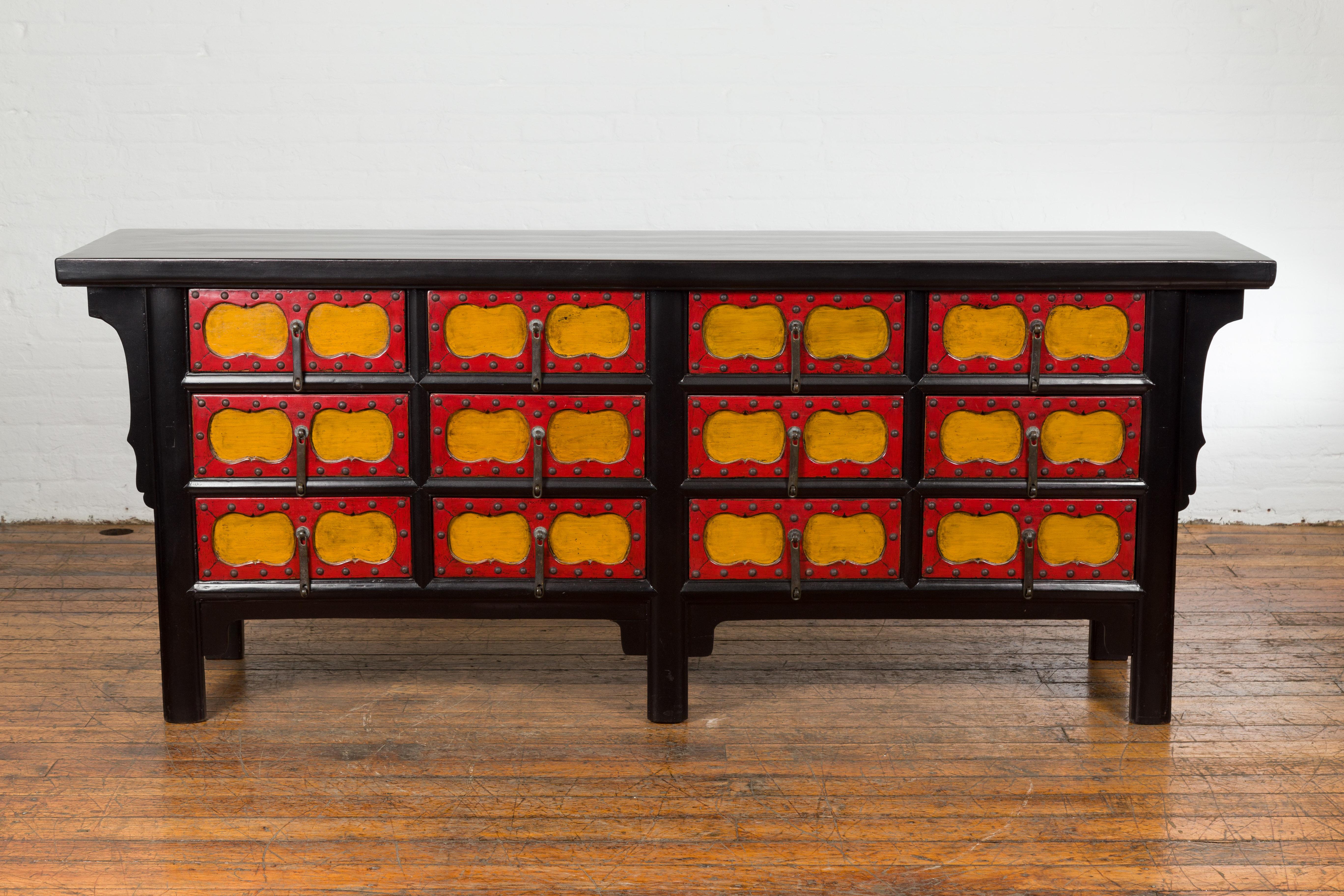 A Chinese Qing Dynasty period long sideboard from the 19th century with black lacquer structure, 12 drawers adorned with yellow recessed cartouches surrounded by red lacquer frames. Experience the timeless sophistication of 19th-century Chinese