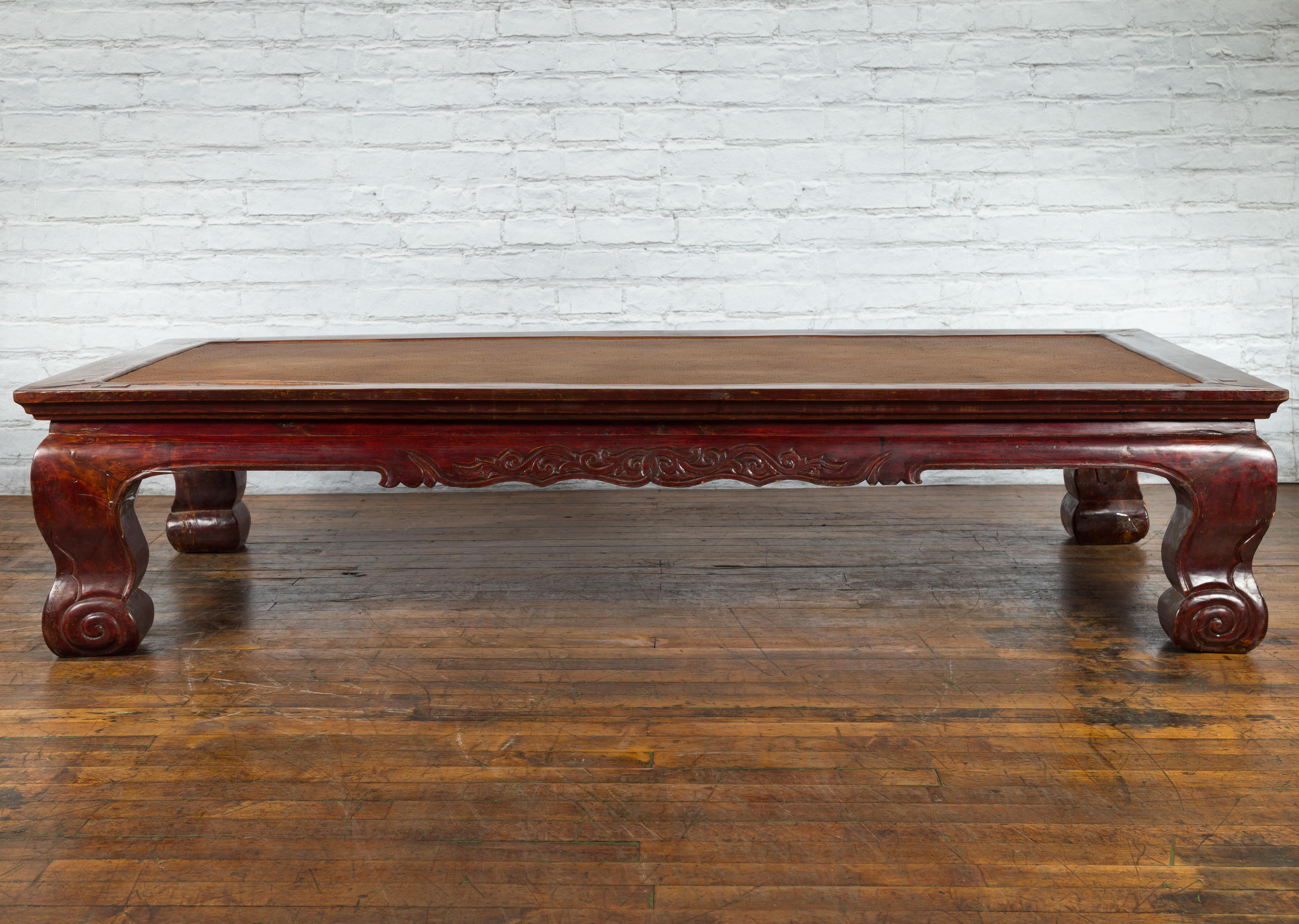 A large Chinese Qing Dynasty period mahogany stained coffee table from the 19th century, with rattan top, carved apron and scrolling legs. Created in China during the Qing Dynasty period in the 19th century, this large coffee table features a