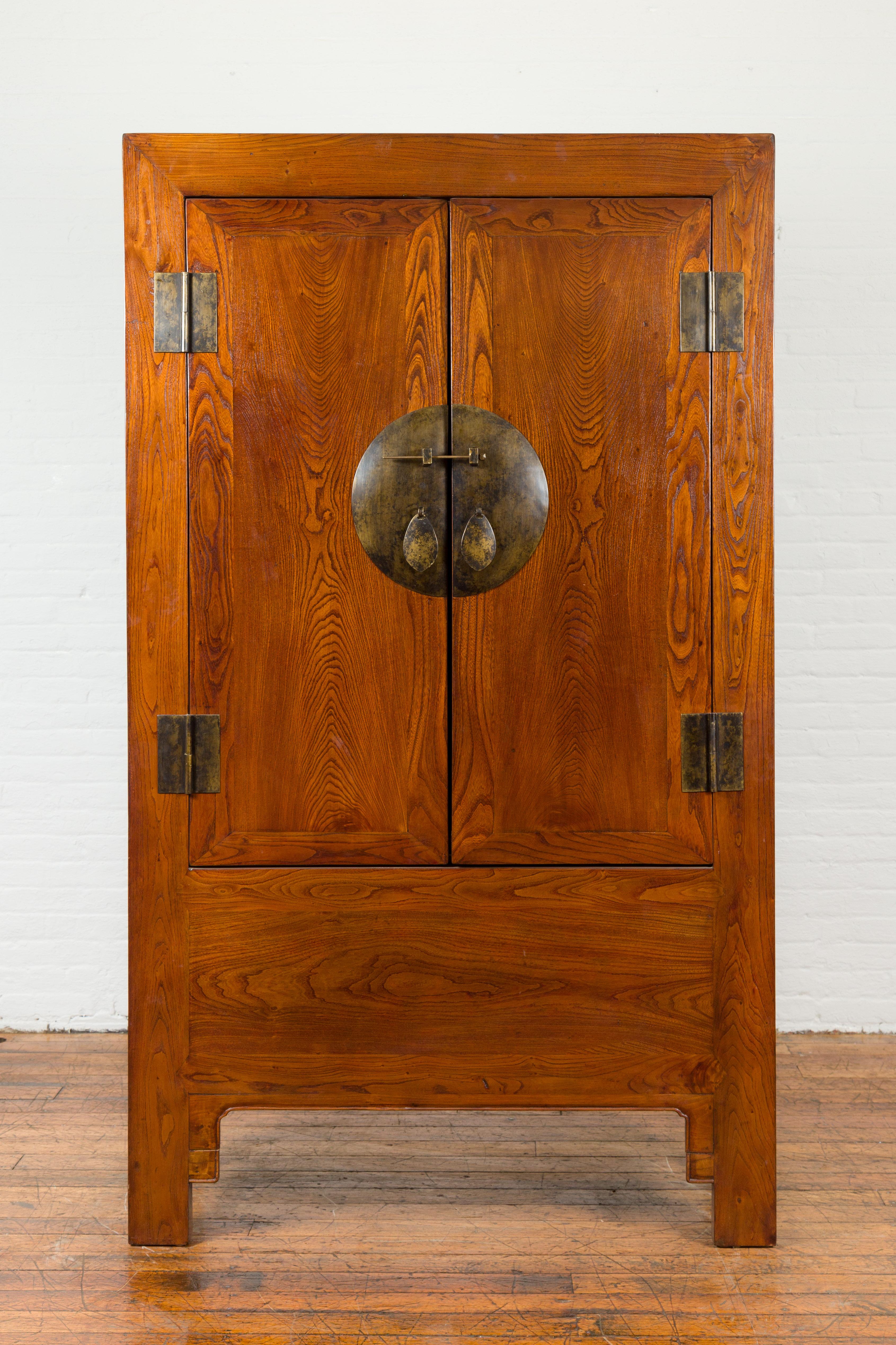 A Chinese Qing Dynasty period nicely grained cabinet from the 19th century, with medallion hardware. Created in China during the Qing Dynasty, this wooden cabinet features a linear silhouette perfectly complimented by a warm brown patina. The façade