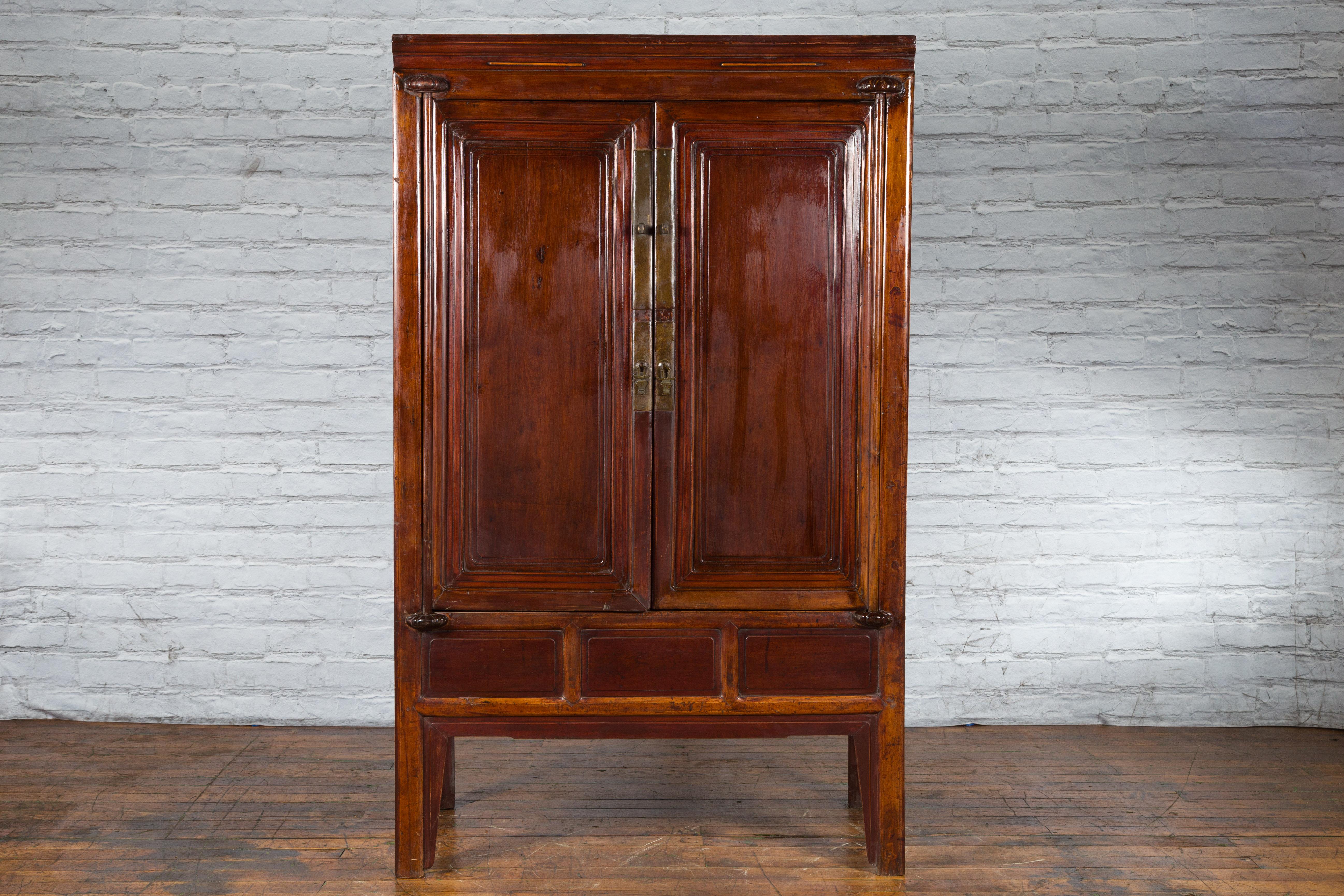 A Chinese Qing dynasty period ningbo cypress cabinet from the 19th century with brass hardware. Created in China during the Qing Dynasty in the 19th century, this ningbo cabinet features a linear silhouette perfectly complimented by a dark brown