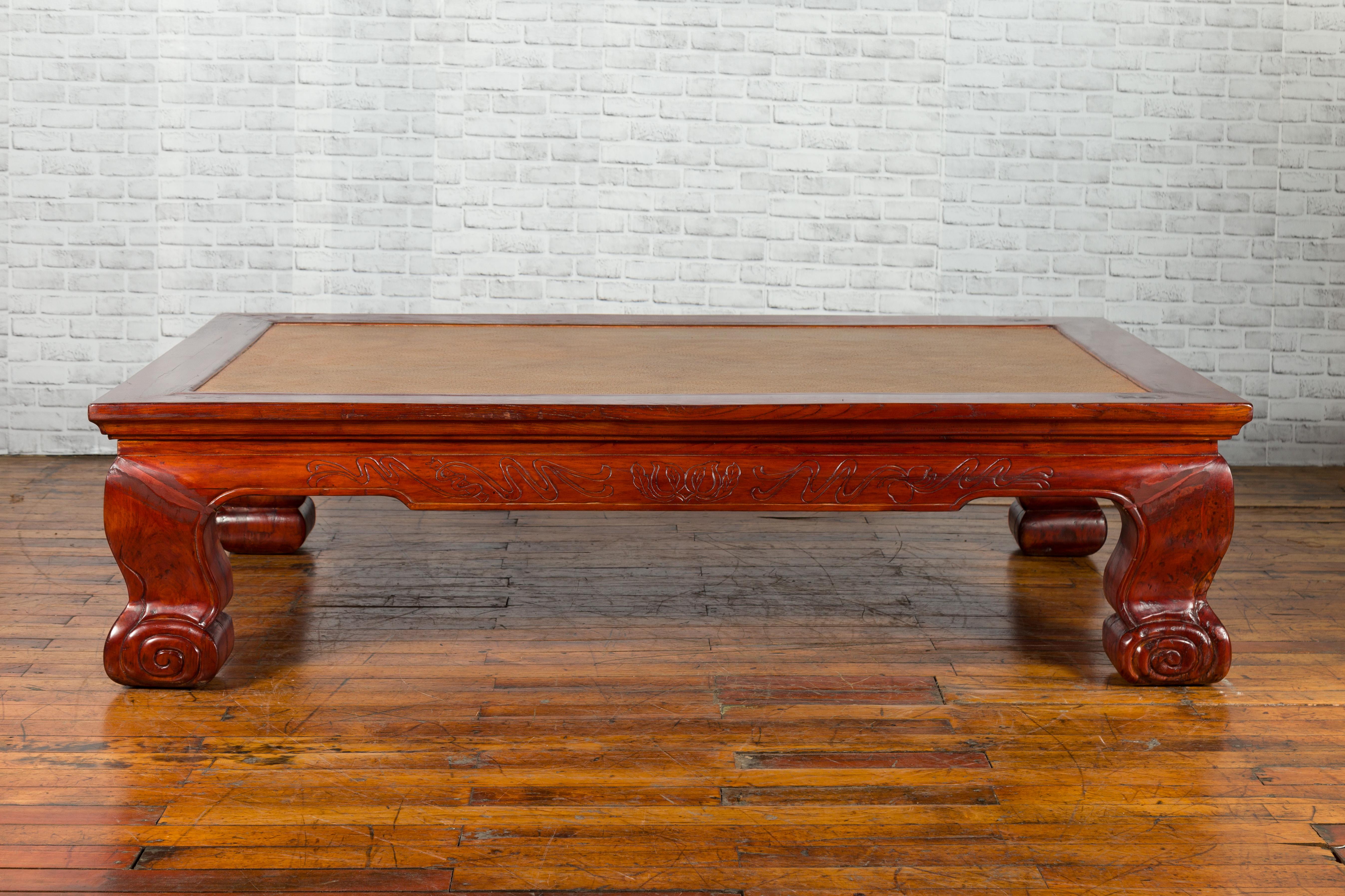 A Chinese Qing Dynasty period opium mat coffee table from the 19th century, with woven rattan top, carved motifs and scrolling legs. Created in China during the Qing Dynasty, this low opium mat coffee table features a woven rattan top secured in a