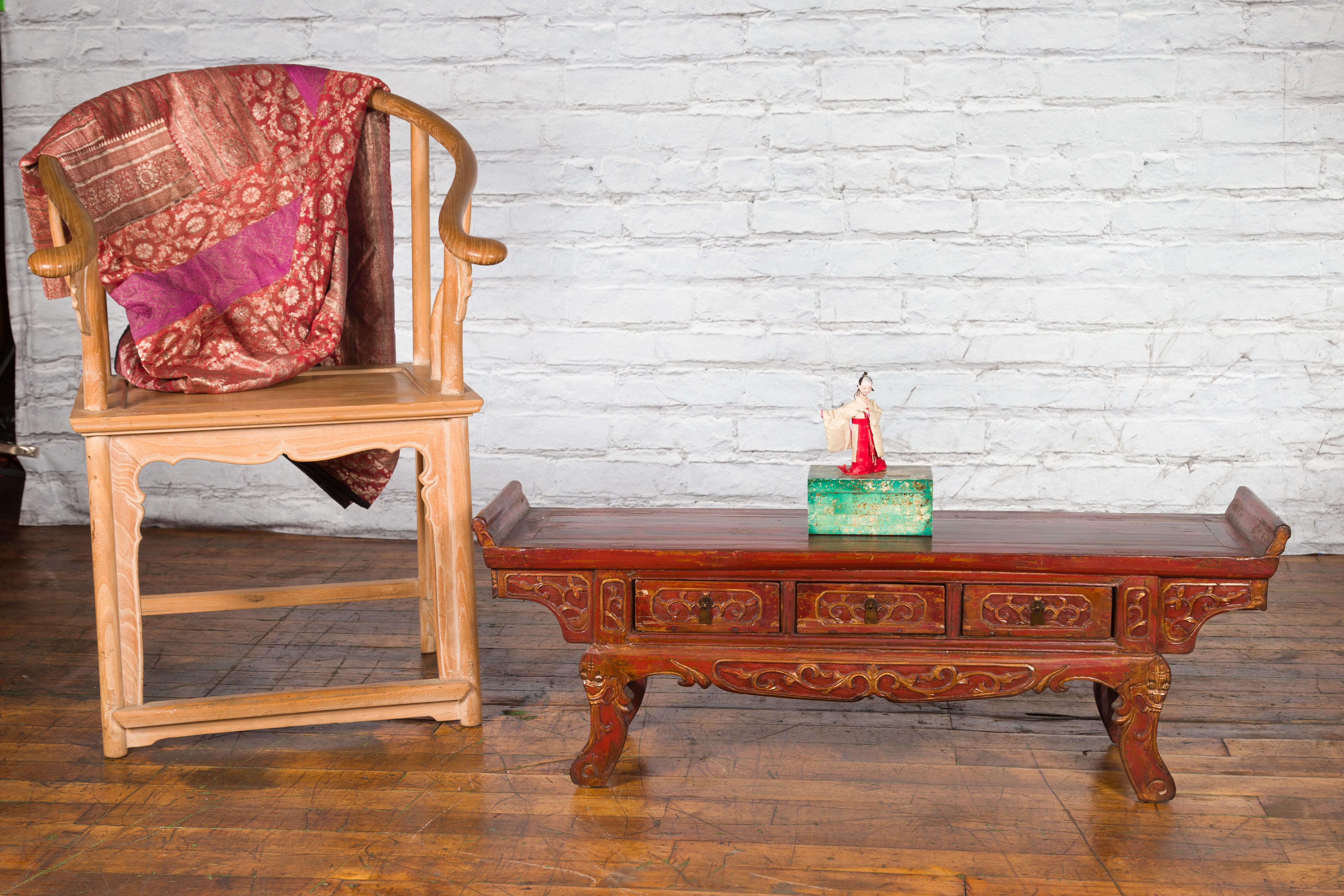 A Chinese Qing Dynasty period ornate red lacquered low altar table from the 19th century, with three drawers, gilt accents and scrolling motifs. Created in China during the Qing Dynasty, this low altar table features a rectangular top with everted