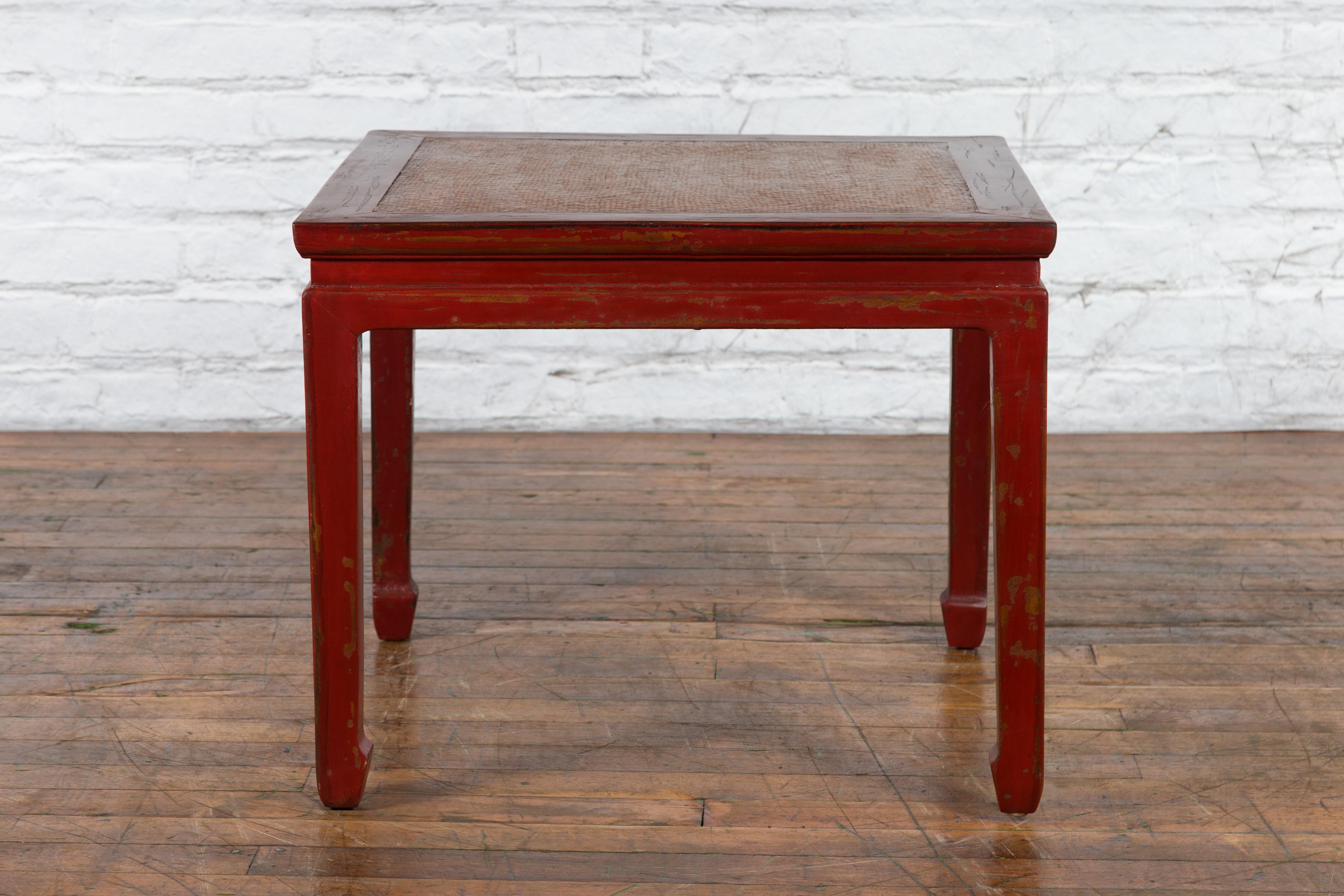 A Chinese Qing Dynasty period side table from the 19th century, with red lacquer, woven rattan top, horse hoof legs and waisted apron. Created in China during the Qing Dynasty period in the 19th century, this side table features a square top