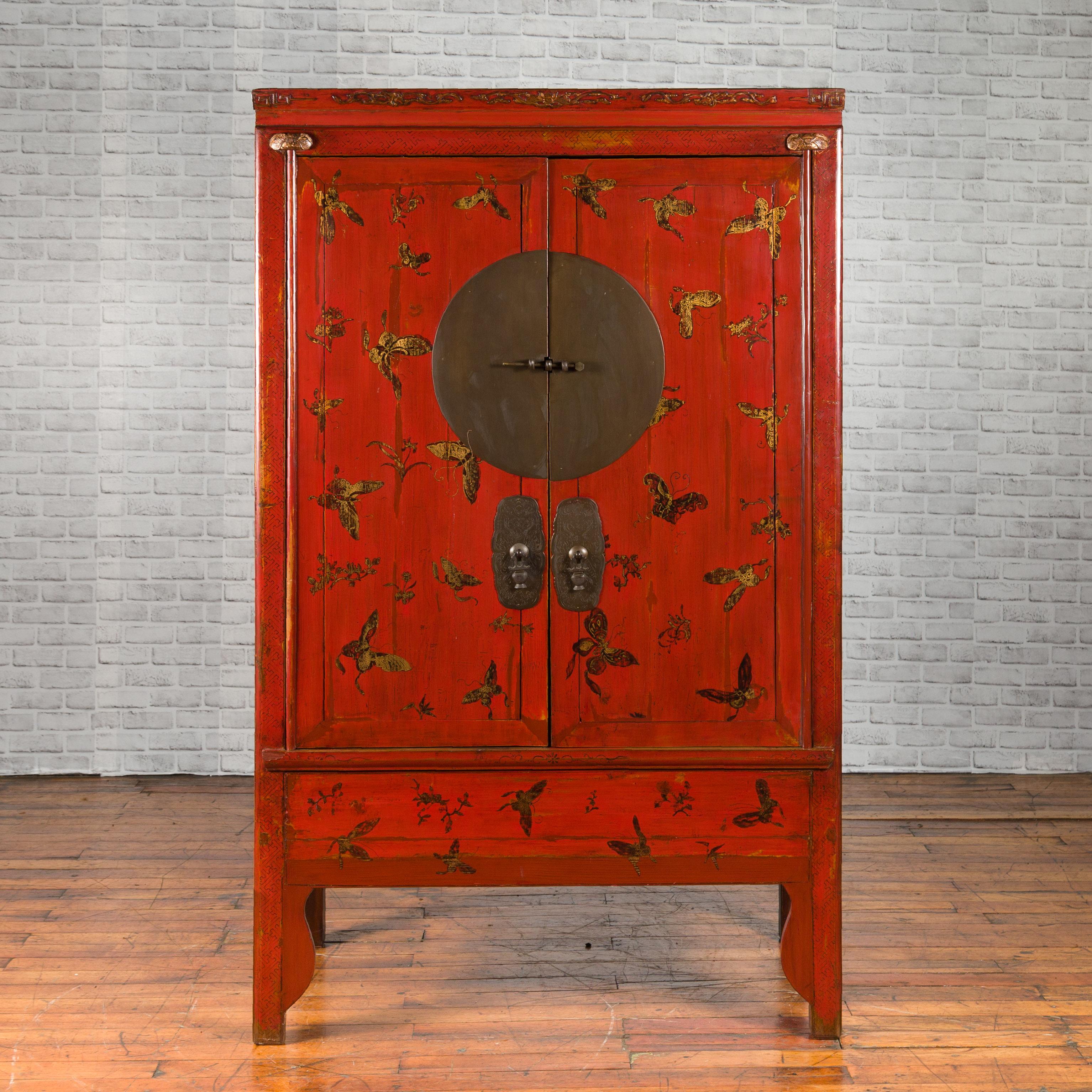 A Chinese Qing Dynasty wedding cabinet from the 19th century with hand-painted gilded butterfly décor and large medallion hardware. Created in China during the Qing Dynasty, this wedding cabinet features a linear silhouette highlighted by a stunning