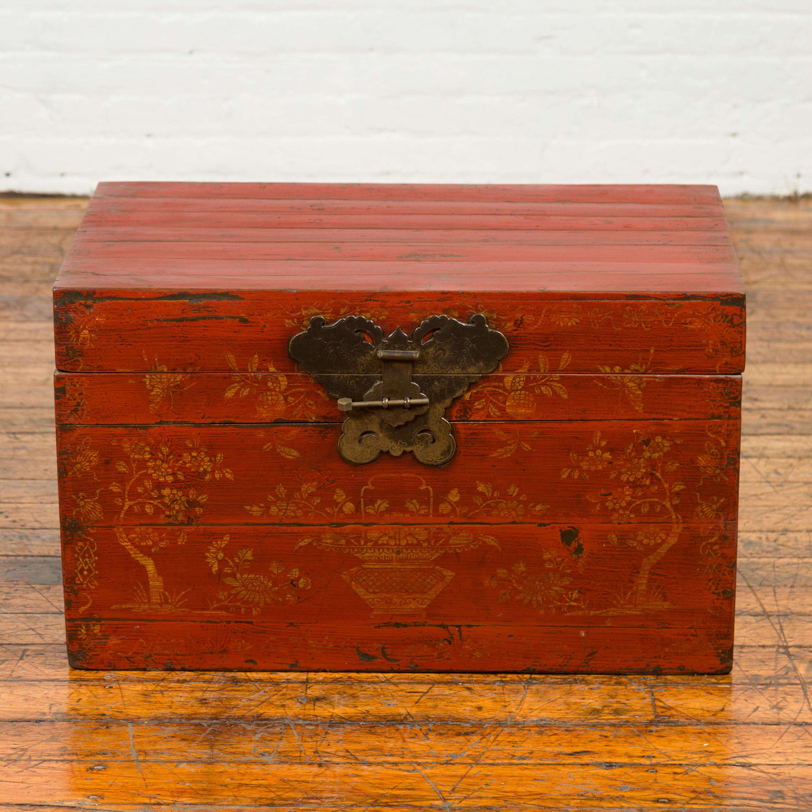 A Chinese Qing red lacquered wooden blanket chest from the 19th century, with floral décor and butterfly brass hardware. Born in China during the Qing Dynasty, this red lacquered blanket chest features a rectangular lid accented with an exquisite