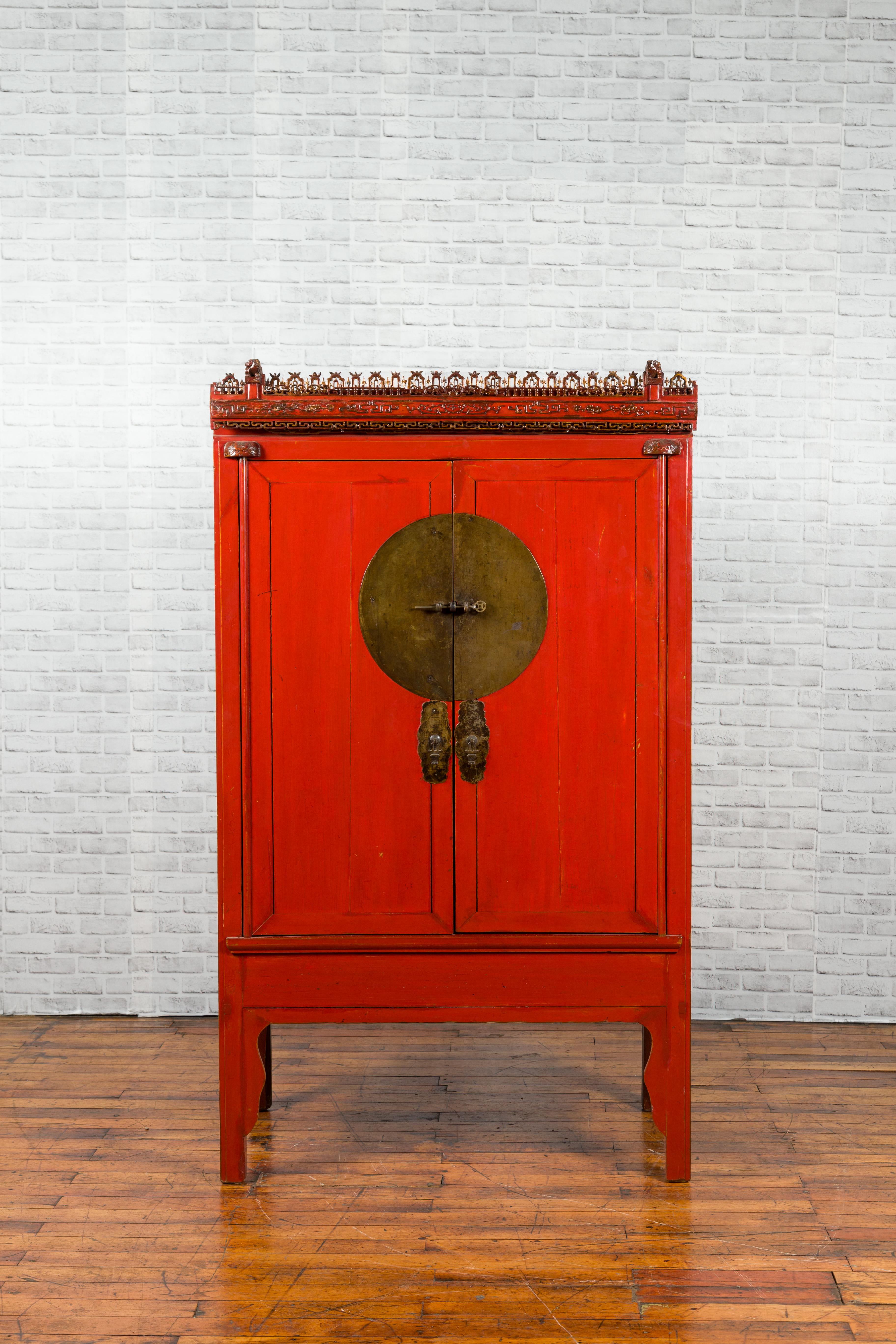 A Chinese Qing Dynasty period red lacquered wedding cabinet from the 19th century, with carved cornice. Created in China during the Qing Dynasty, this red lacquered cabinet features two simple doors opening thanks to a large brass medallion to