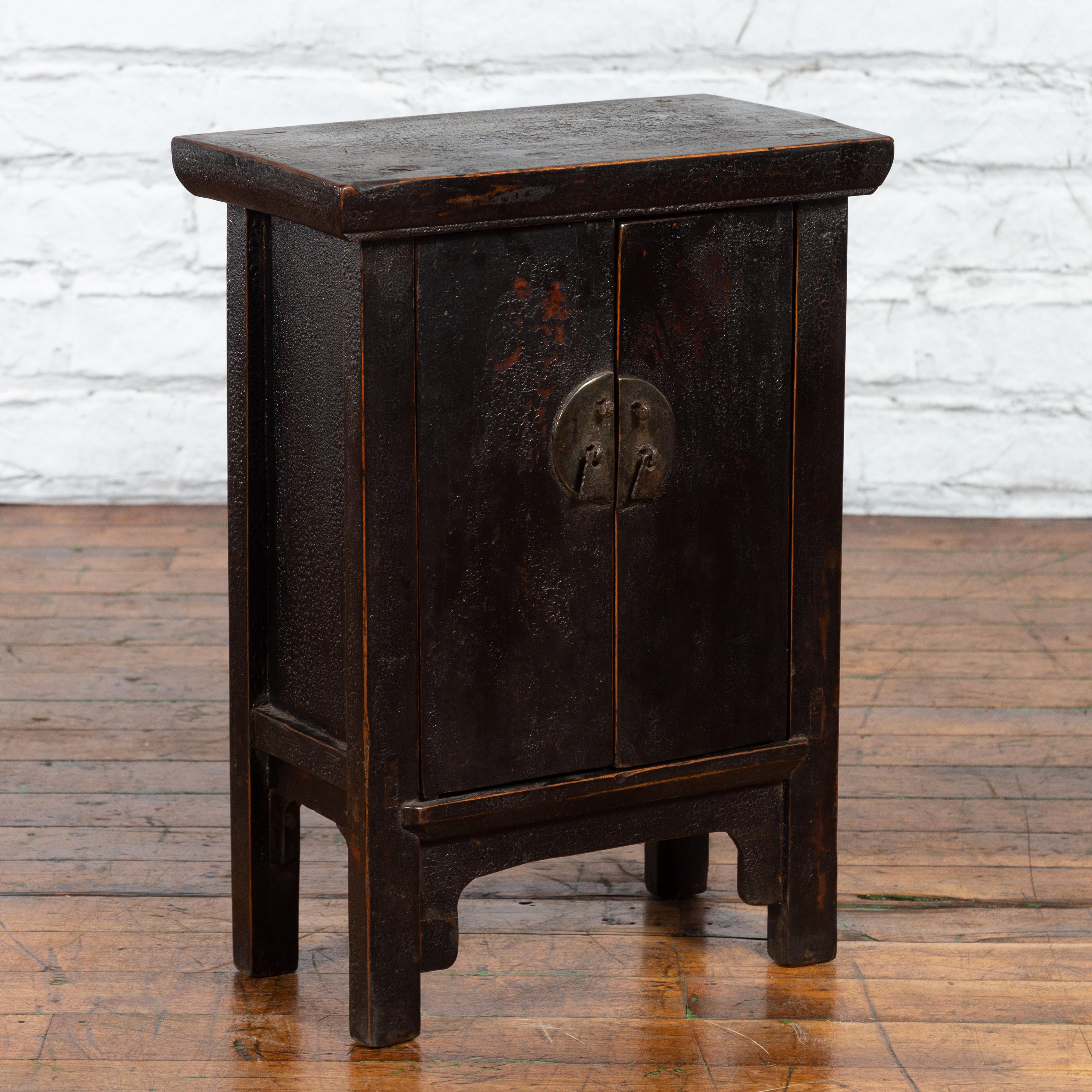 A Chinese Qing Dynasty period side cabinet from the 19th century with double doors, distressed black lacquer and brass hardware. Created in China during the Qing Dynasty in the 19th century, this side cabinet features a rectangular top with slightly
