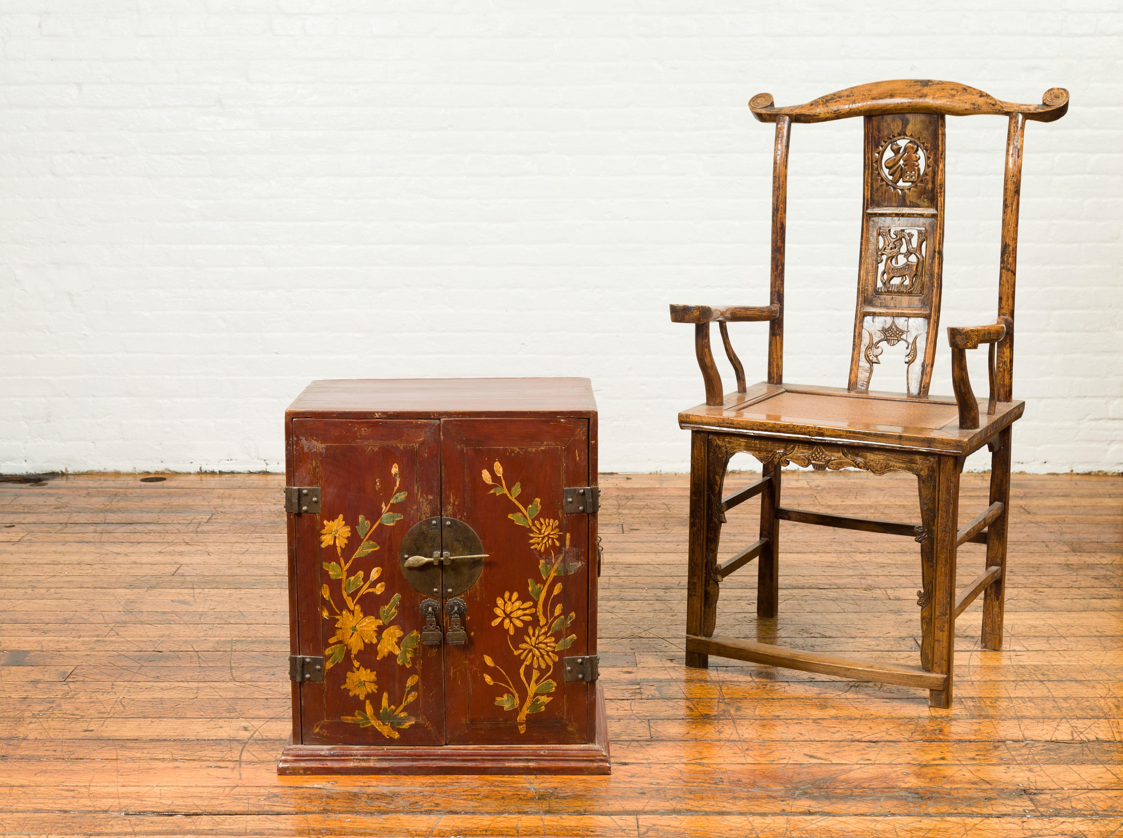 A Chinese Qing dynasty brown / dark red wooden side cabinet from the 19th century, with painted floral decor, bronze hardware and hidden drawers. This Qing Dynasty side cabinet, originating from 19th-century China, is a masterpiece of artistry and