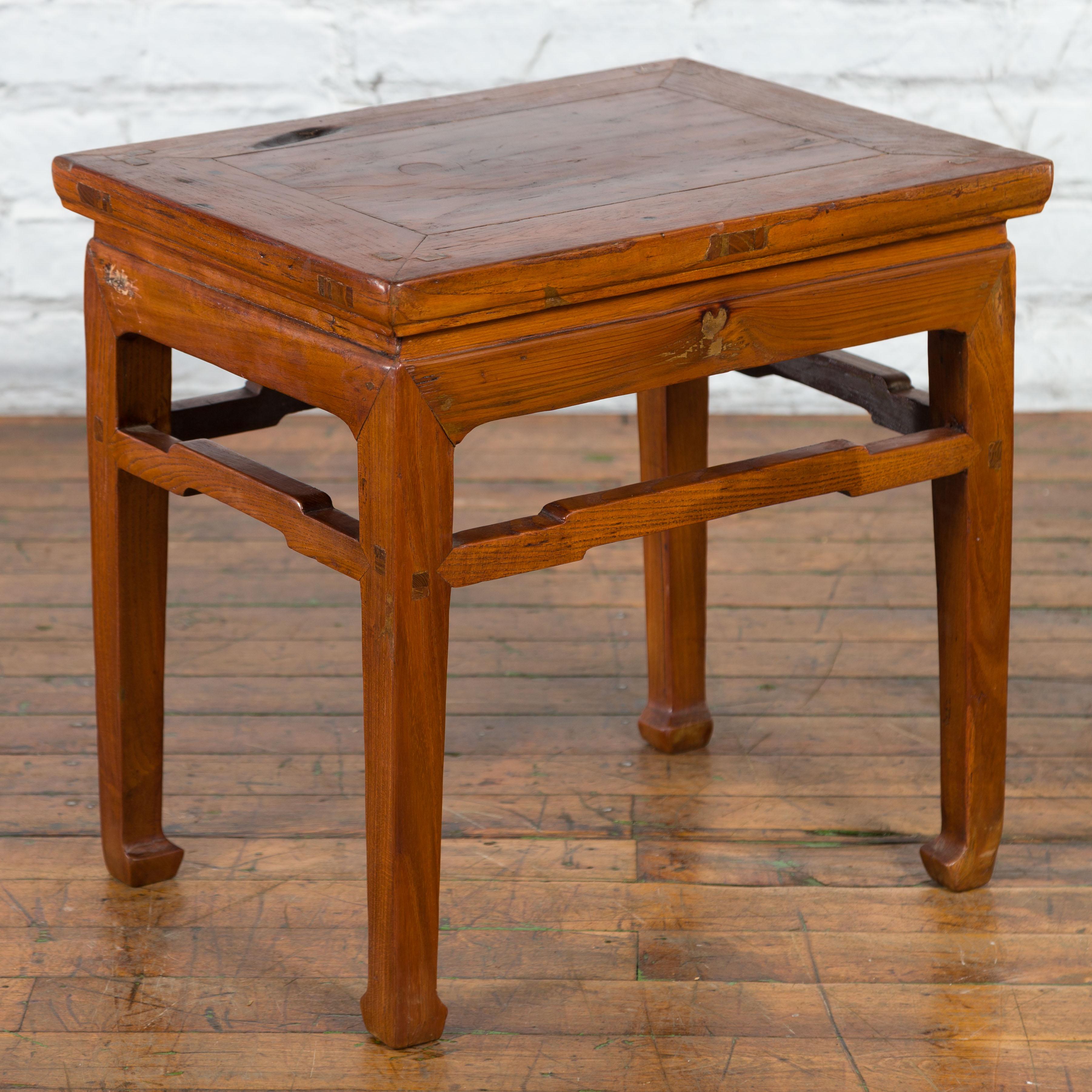 A Chinese Qing Dynasty period side table from the 19th century with waisted apron, humpback stretcher, horse hoof feet and natural patina. Created in China during the Qing Dynasty period in the 19th century, this side table features a rectangular