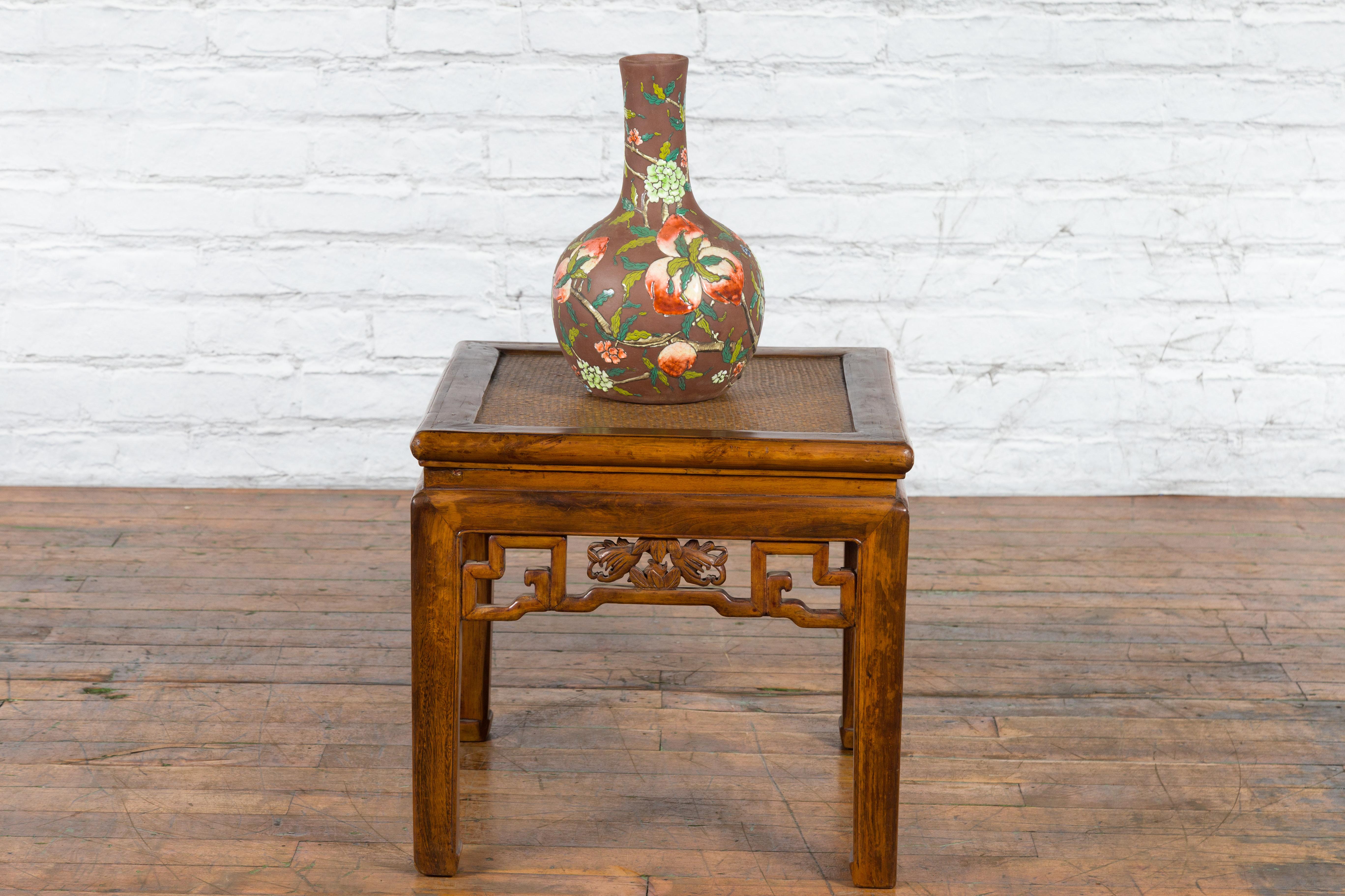 A Chinese Qing Dynasty period side table from the 19th century, with woven rattan mat, fretwork apron and carved foliage. Created in China during the Qing Dynasty period in the 19th century, this side table features a square waisted top with central