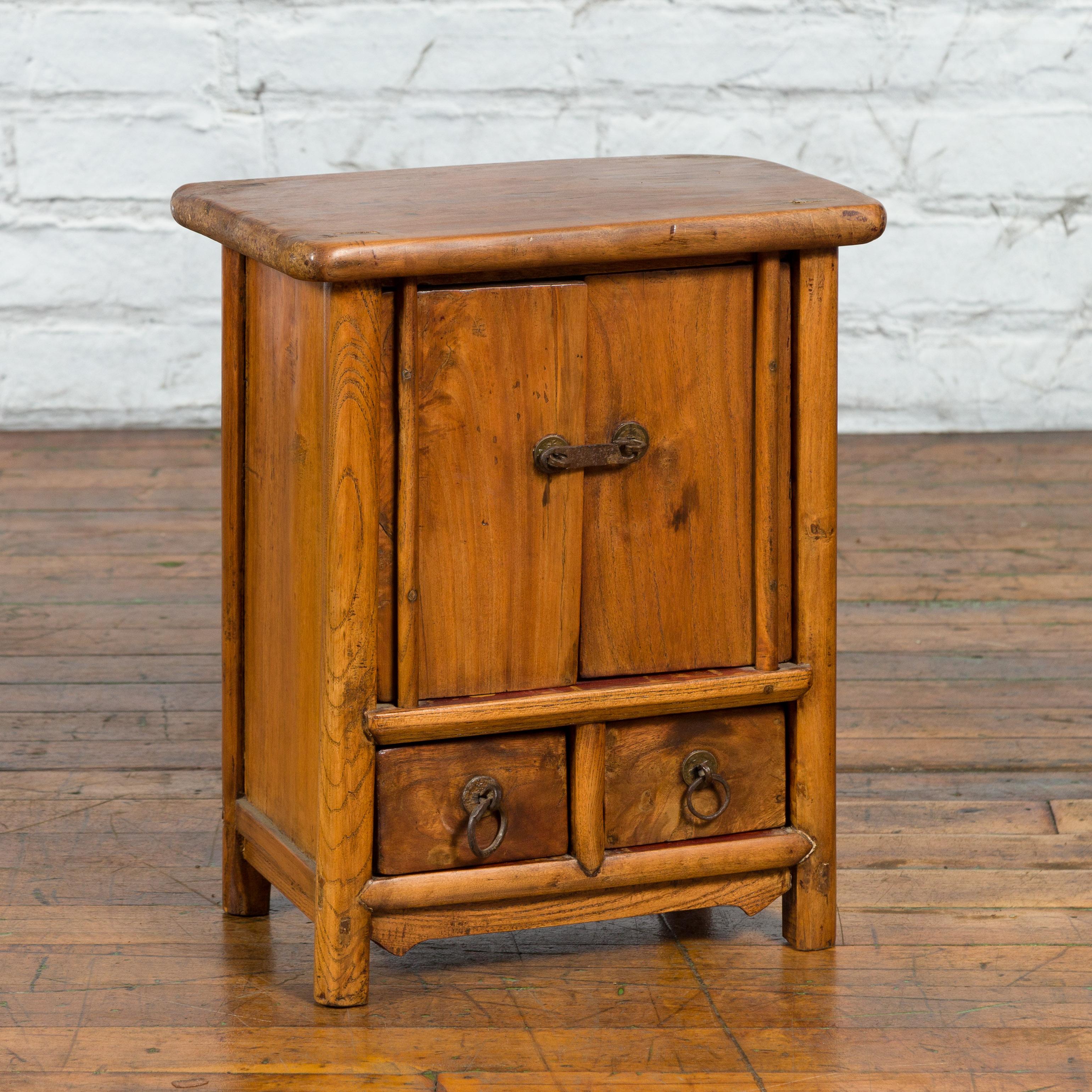A small Chinese Qing Dynasty elmwood tapering bedside cabinet from the 19th century, with two doors and two drawers. Created in China during the Qing Dynasty, this elmwood bedside cabinet features a rectangular top sitting above two doors fitted
