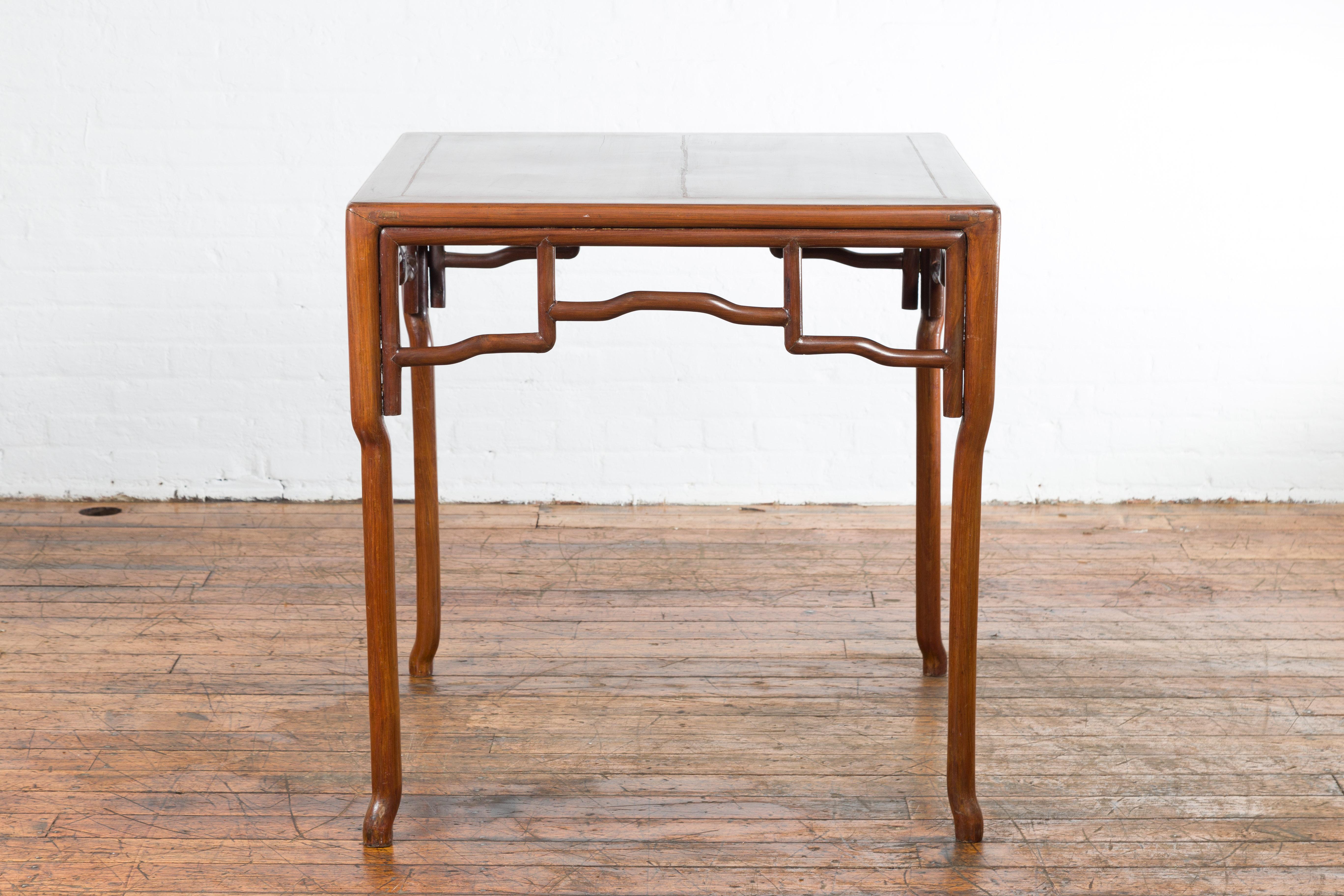 A Chinese Qing Dynasty period square top wooden game table from the 19th century with openwork apron and curving legs. Created in China during the Qing Dynasty, this game table features a square top with central board, sitting above an elegant
